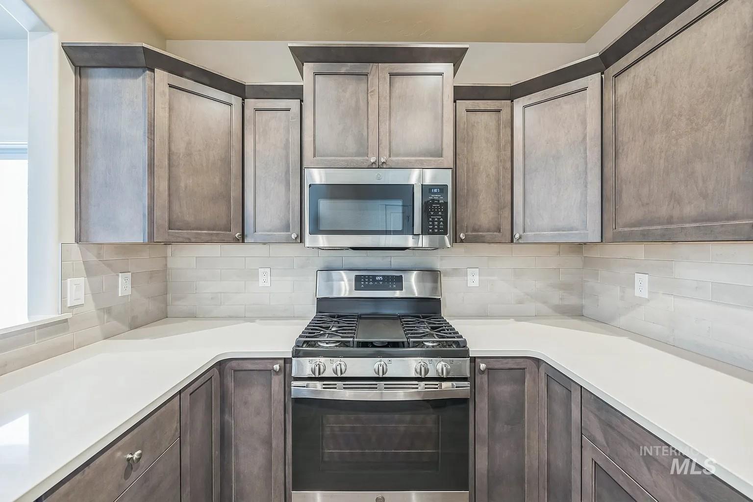 Kitchen featuring a stainless steel range with overhead microwave, light-toned cabinetry, white countertops, and a subway tile backsplash