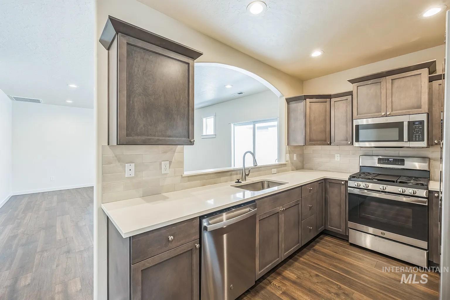 Kitchen featuring wood-finish flooring, stainless steel appliances, light countertops, and an arched pass-through window
