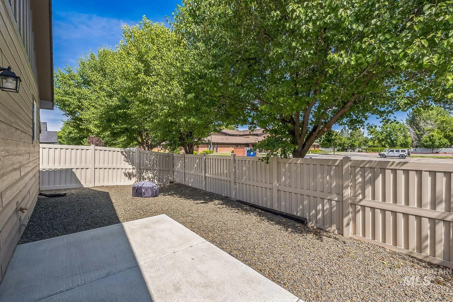 Enclosed gravel yard featuring a light-toned privacy fence and mature trees
