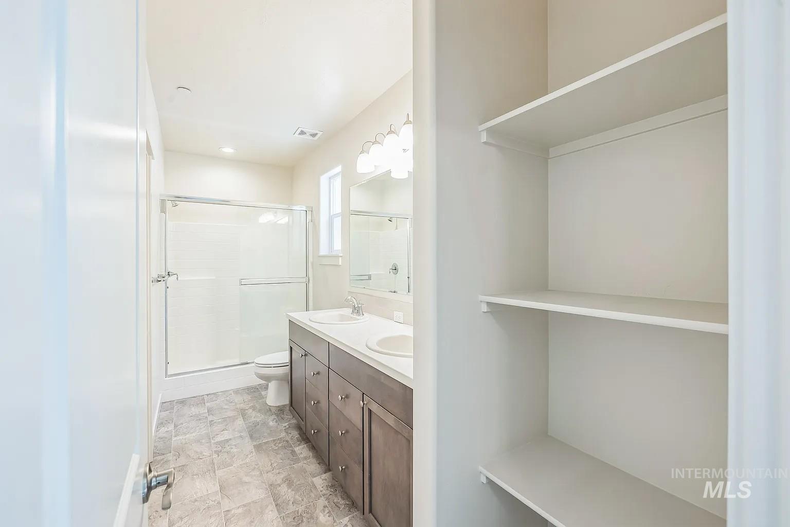 Bathroom featuring a dual-sink vanity with wood-finish cabinetry, a shower with sliding glass doors, and tile flooring