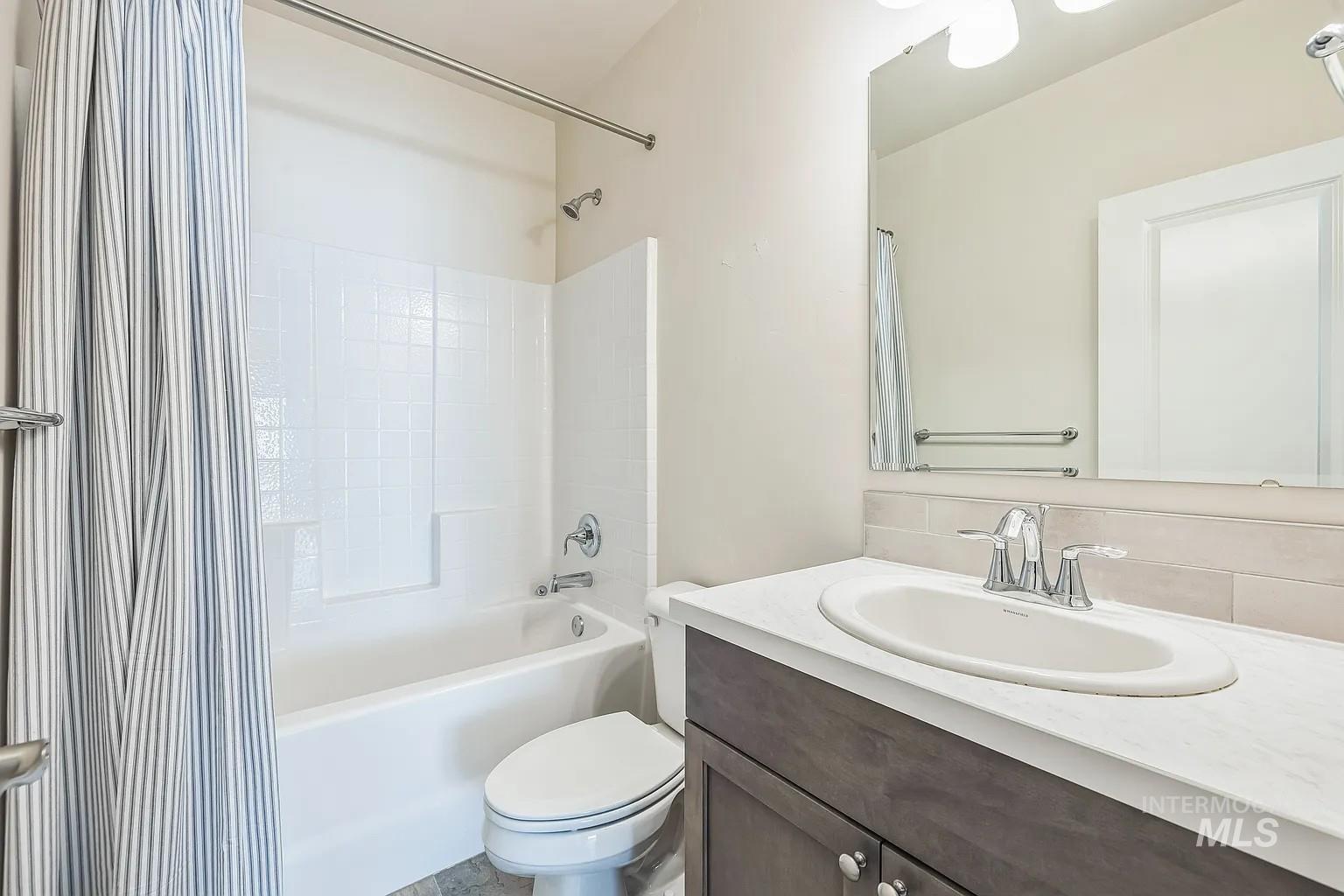 Bathroom featuring a white tub/shower combination with tile surround, a dark wood-finish vanity with a white countertop, an undermount sink, and a framed mirror