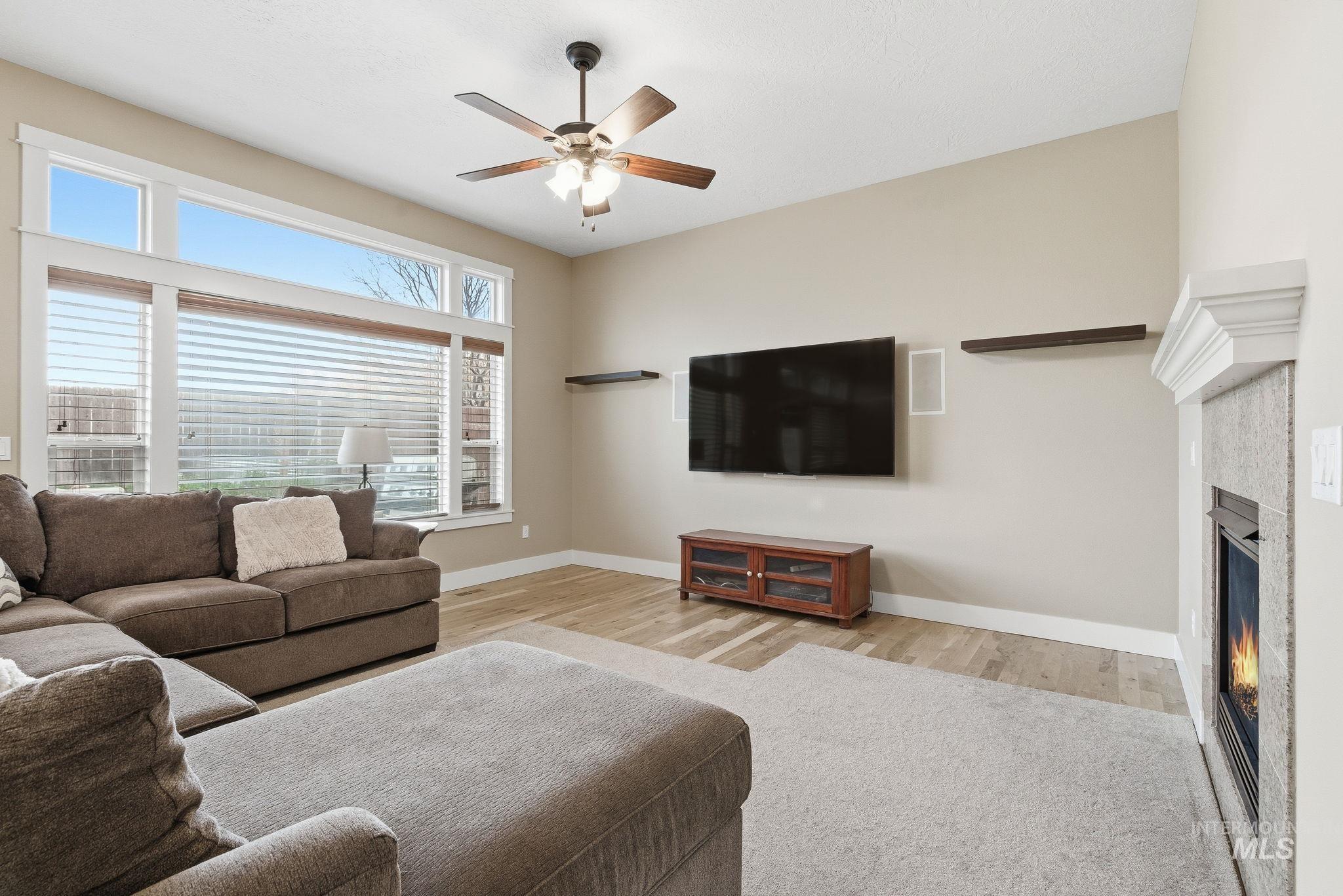 Living room featuring a glass covered fireplace, a ceiling fan, and light wood-type flooring