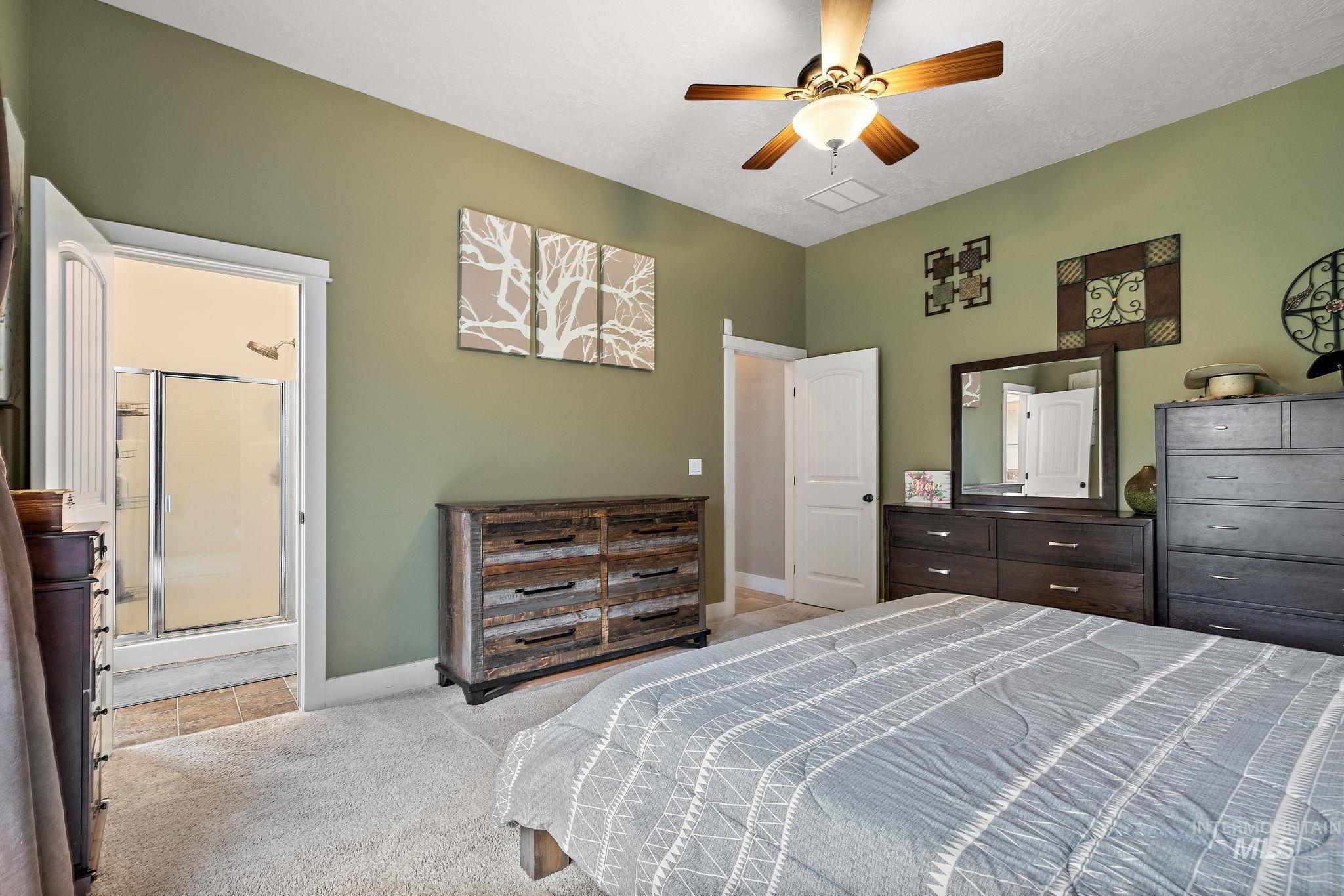 Bedroom with ceiling fan, ensuite bathroom, light carpet, and light tile patterned flooring