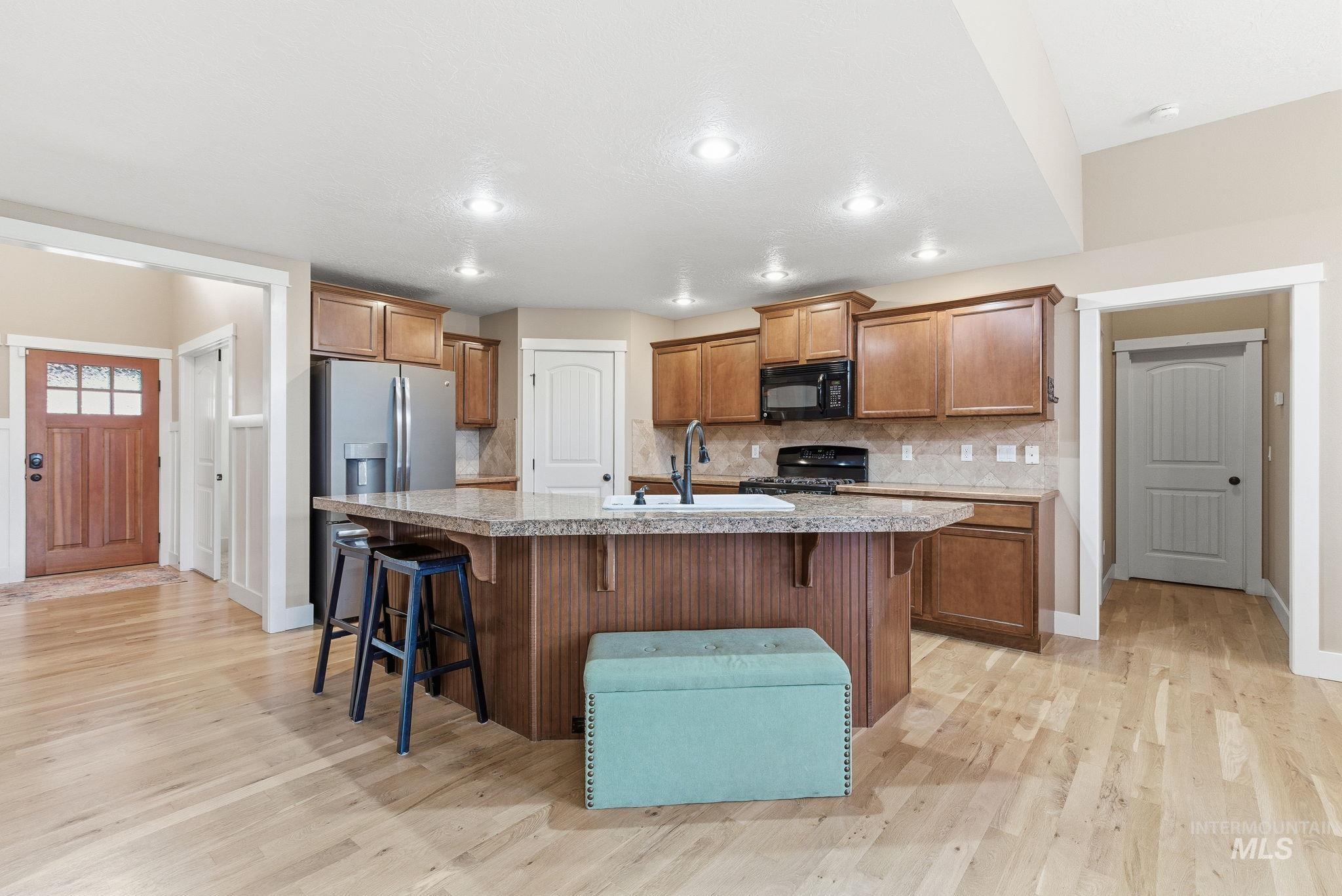 Kitchen featuring a breakfast bar, brown cabinets, decorative backsplash, a center island with sink, and recessed lighting