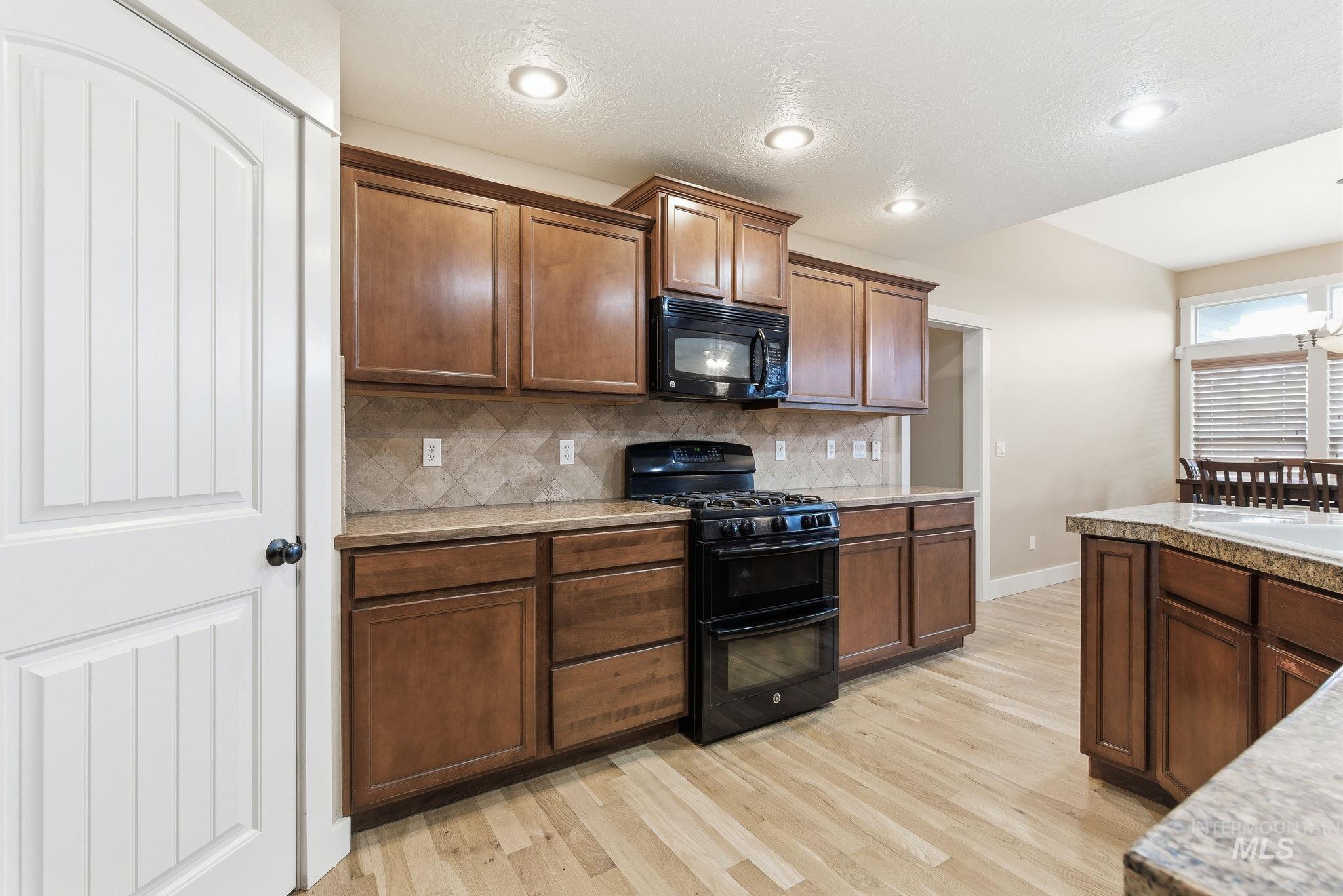 Kitchen featuring black appliances, tasteful backsplash, light wood-style flooring, recessed lighting, and a textured ceiling