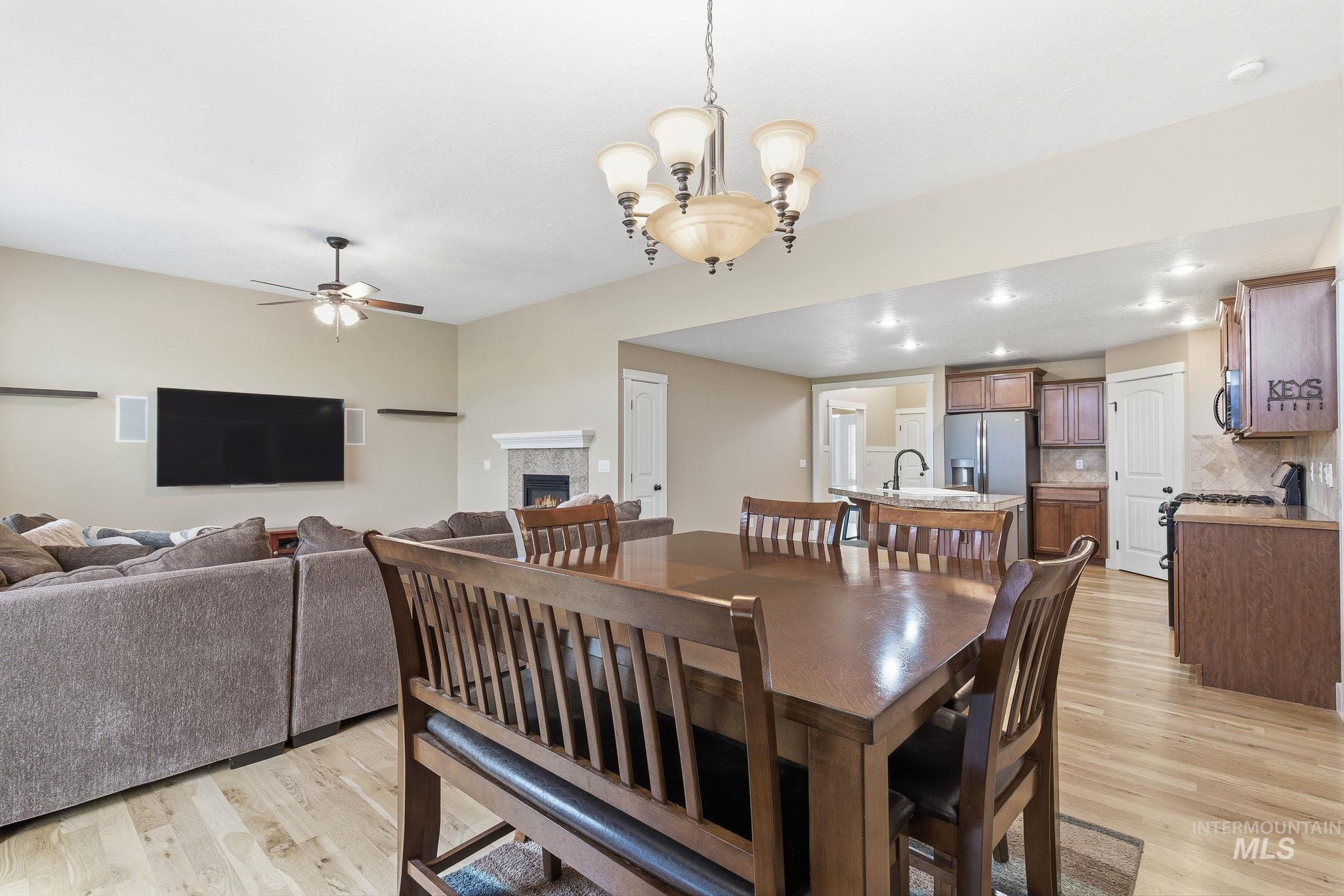 Dining space featuring a warm lit fireplace, light wood finished floors, a chandelier, ceiling fan, and recessed lighting