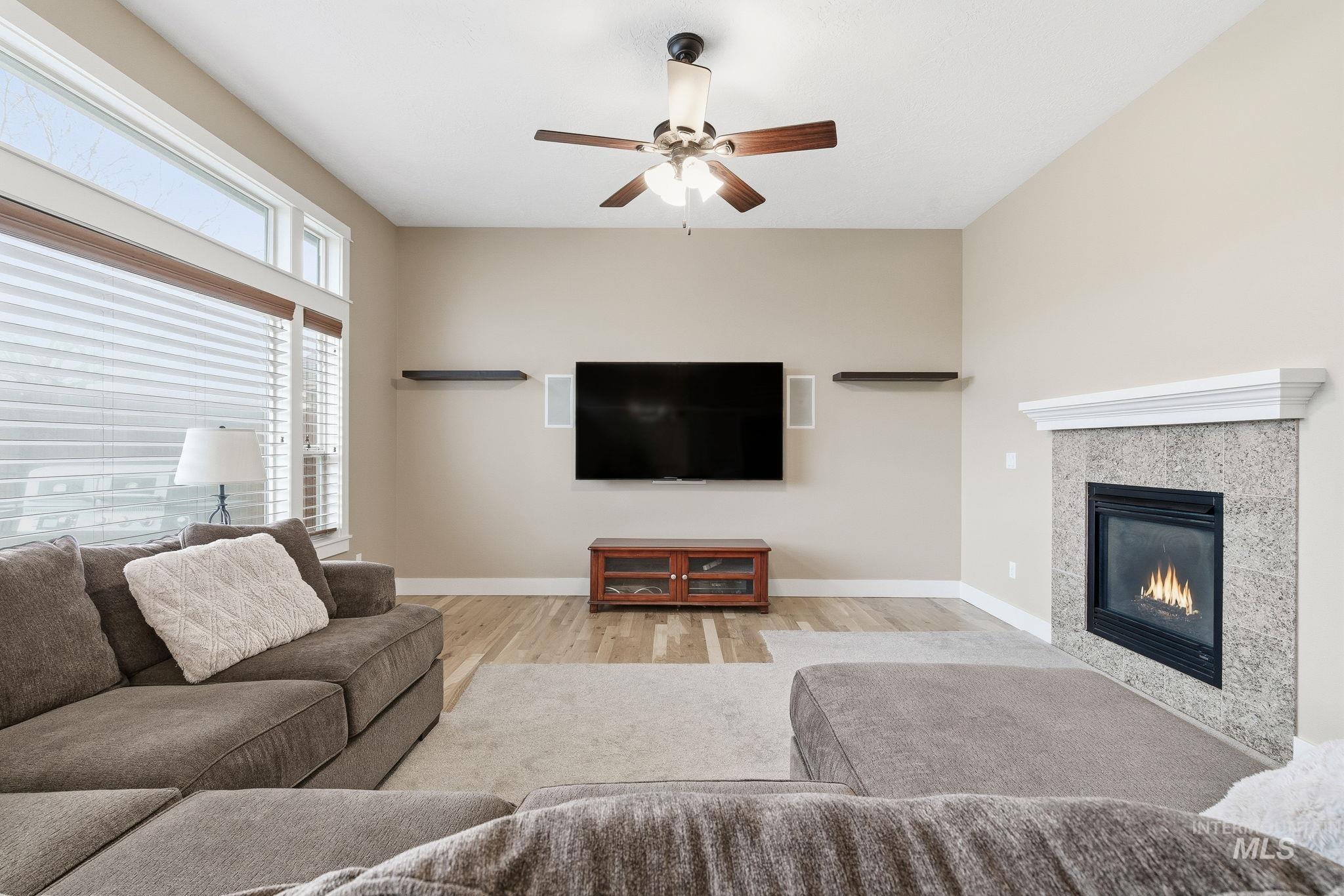Living room with ceiling fan, light wood finished floors, and a tiled fireplace