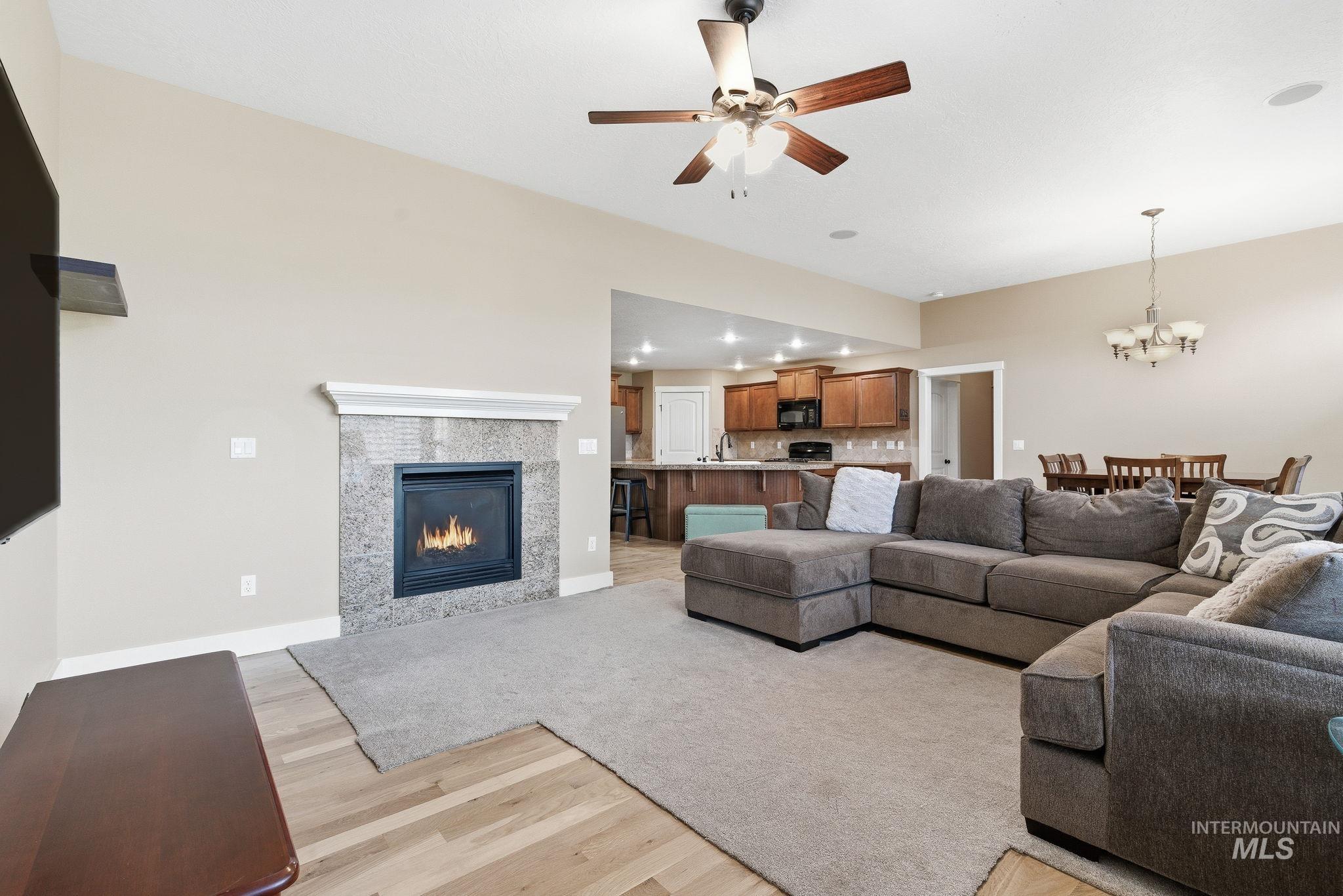 Living room featuring a tile fireplace, light wood-style flooring, a ceiling fan, a chandelier, and recessed lighting