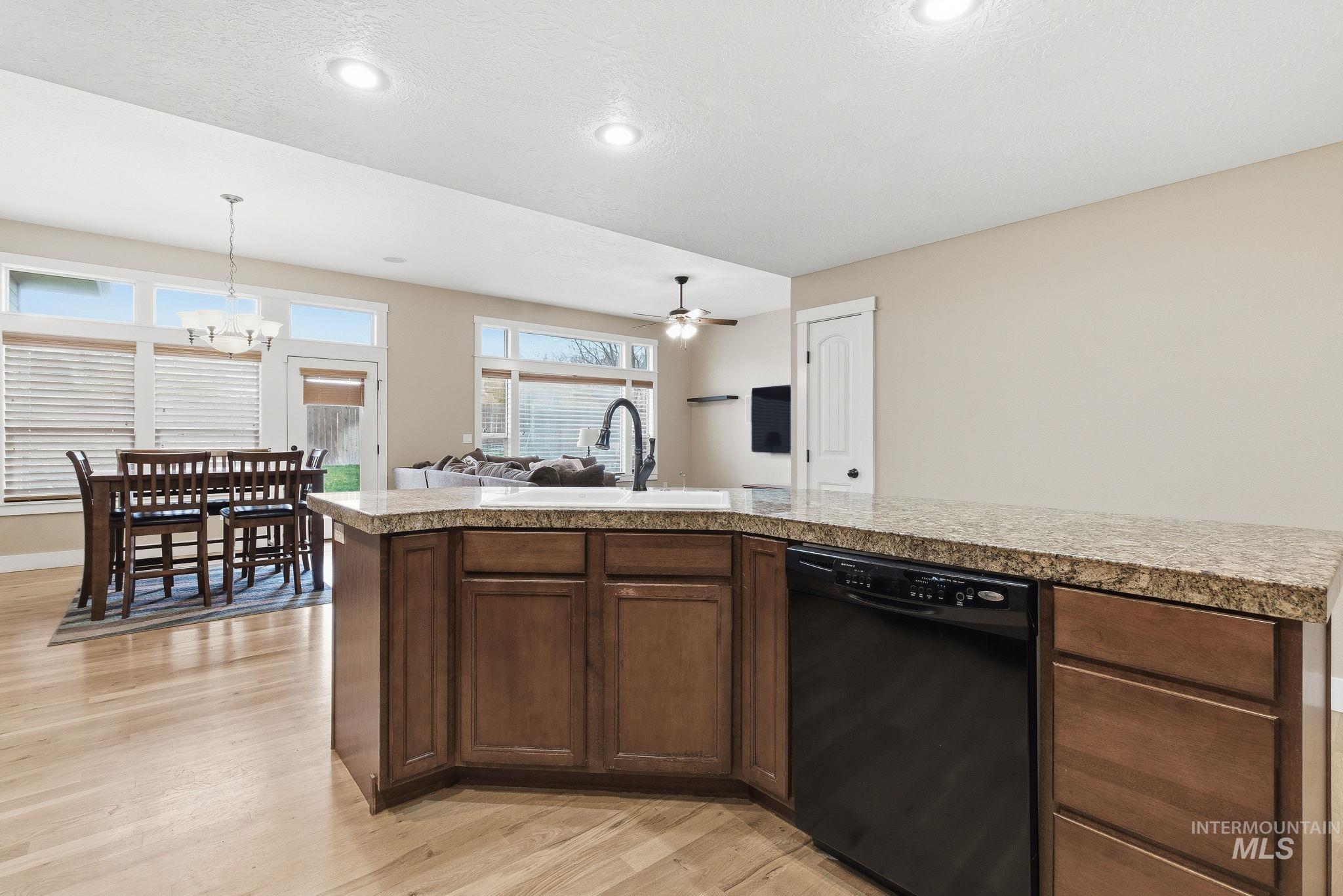 Kitchen featuring tile countertops, dishwasher, open floor plan, light wood-style flooring, and dark brown cabinets