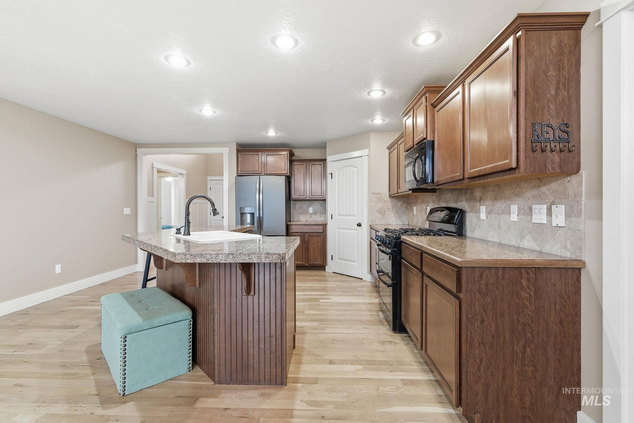 Kitchen featuring a kitchen breakfast bar, tile counters, black appliances, an island with sink, and recessed lighting