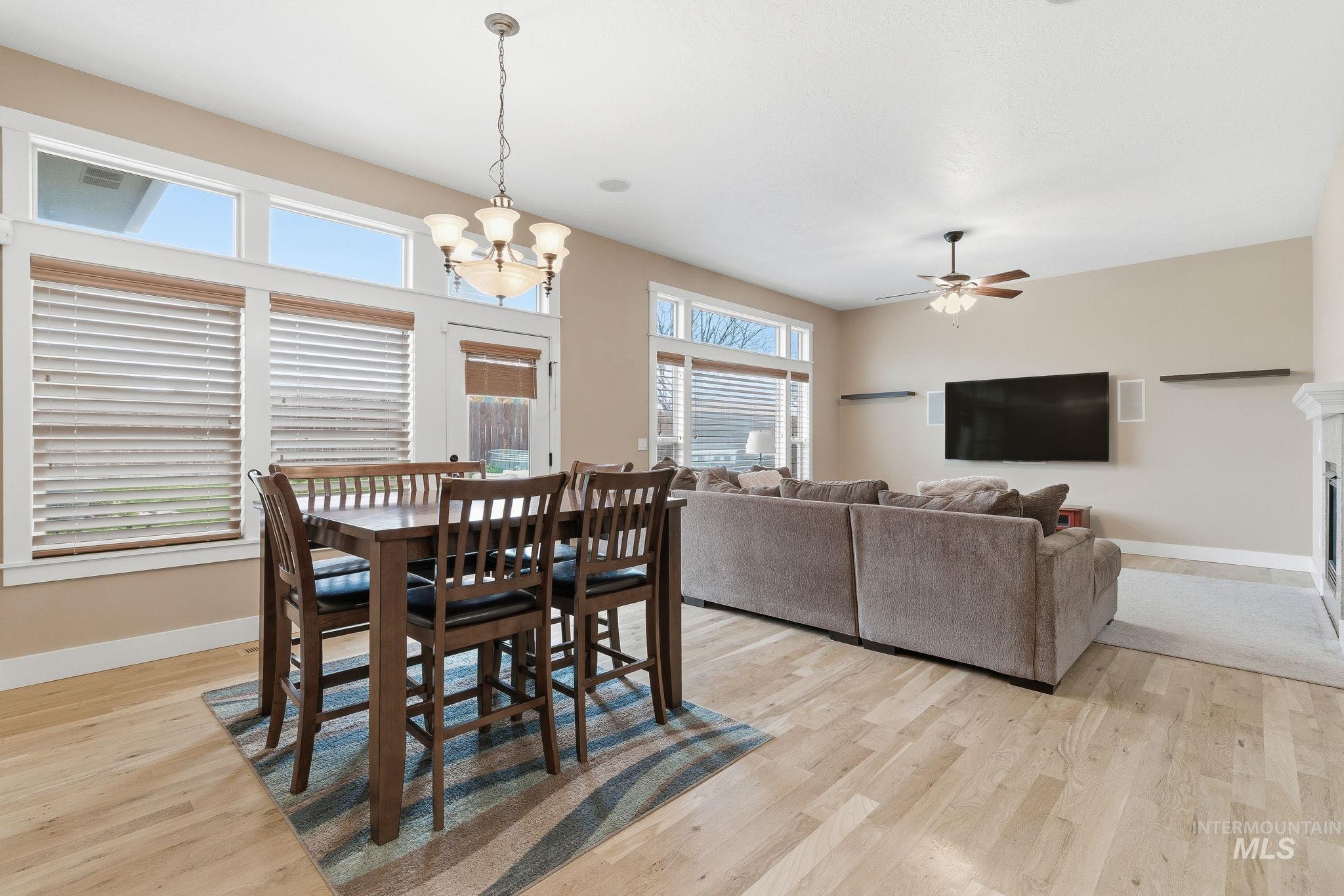 Dining area featuring light wood-style flooring, a chandelier, a fireplace with flush hearth, and ceiling fan