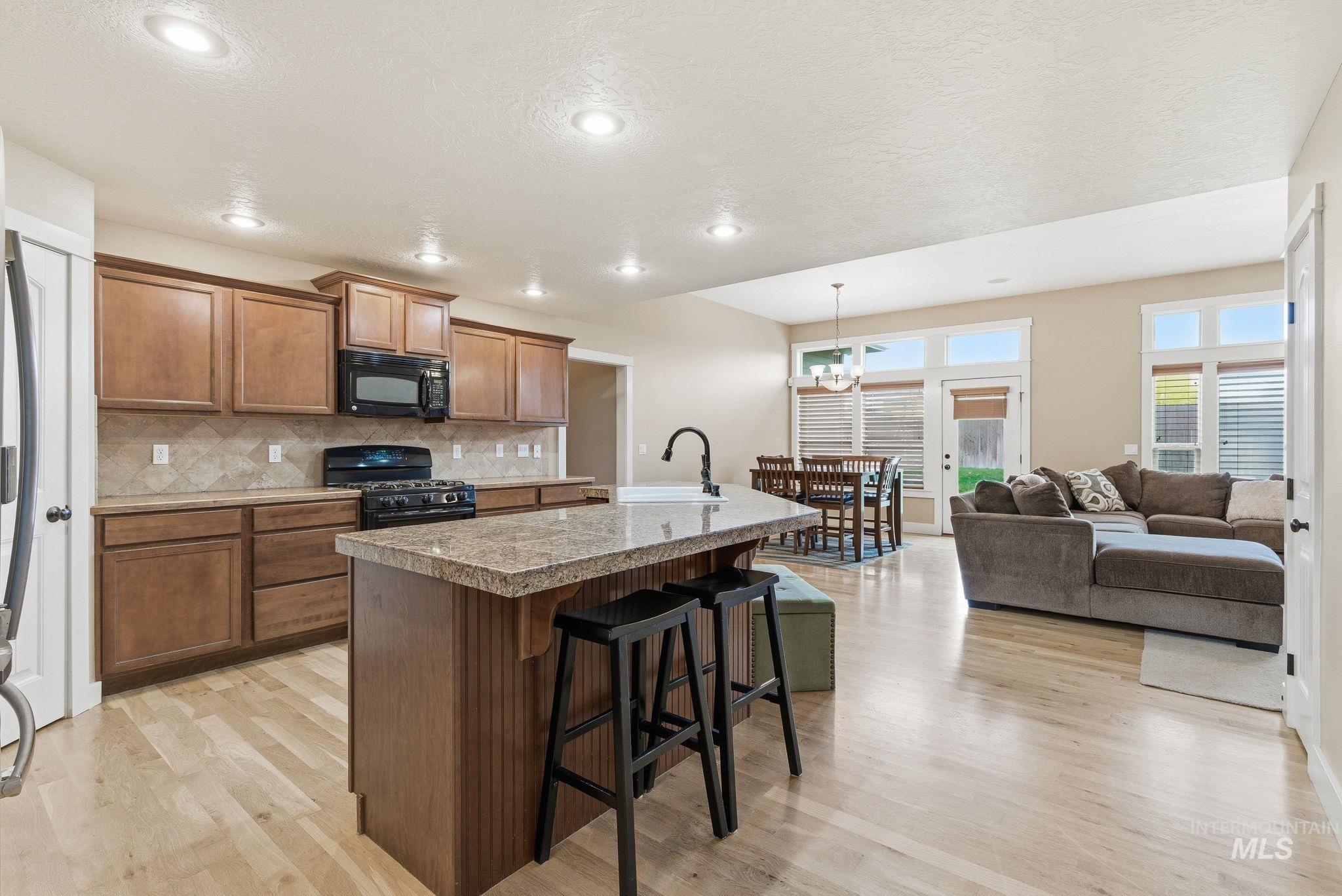 Kitchen featuring a breakfast bar, brown cabinetry, an island with sink, black appliances, and tasteful backsplash