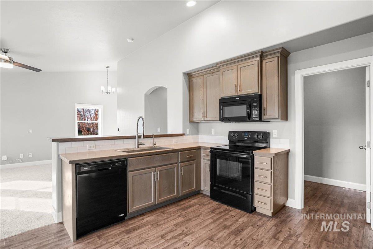 Kitchen featuring black appliances, a peninsula, arched walkways, dark wood-type flooring, and ceiling fan