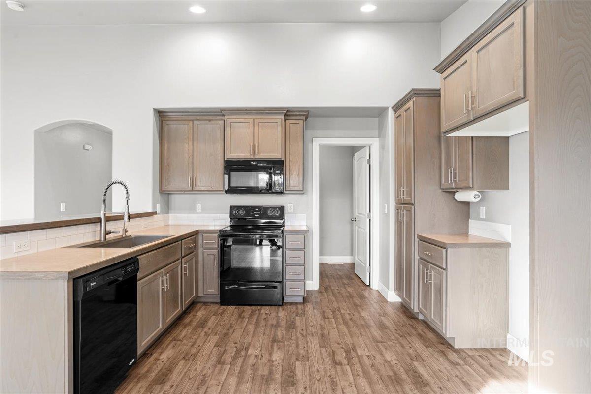 Kitchen with black appliances, light countertops, dark wood-style flooring, recessed lighting, and a peninsula