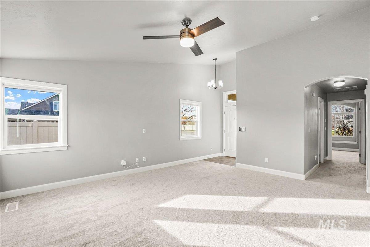 Empty room featuring light carpet, healthy amount of natural light, a ceiling fan, arched walkways, and high vaulted ceiling
