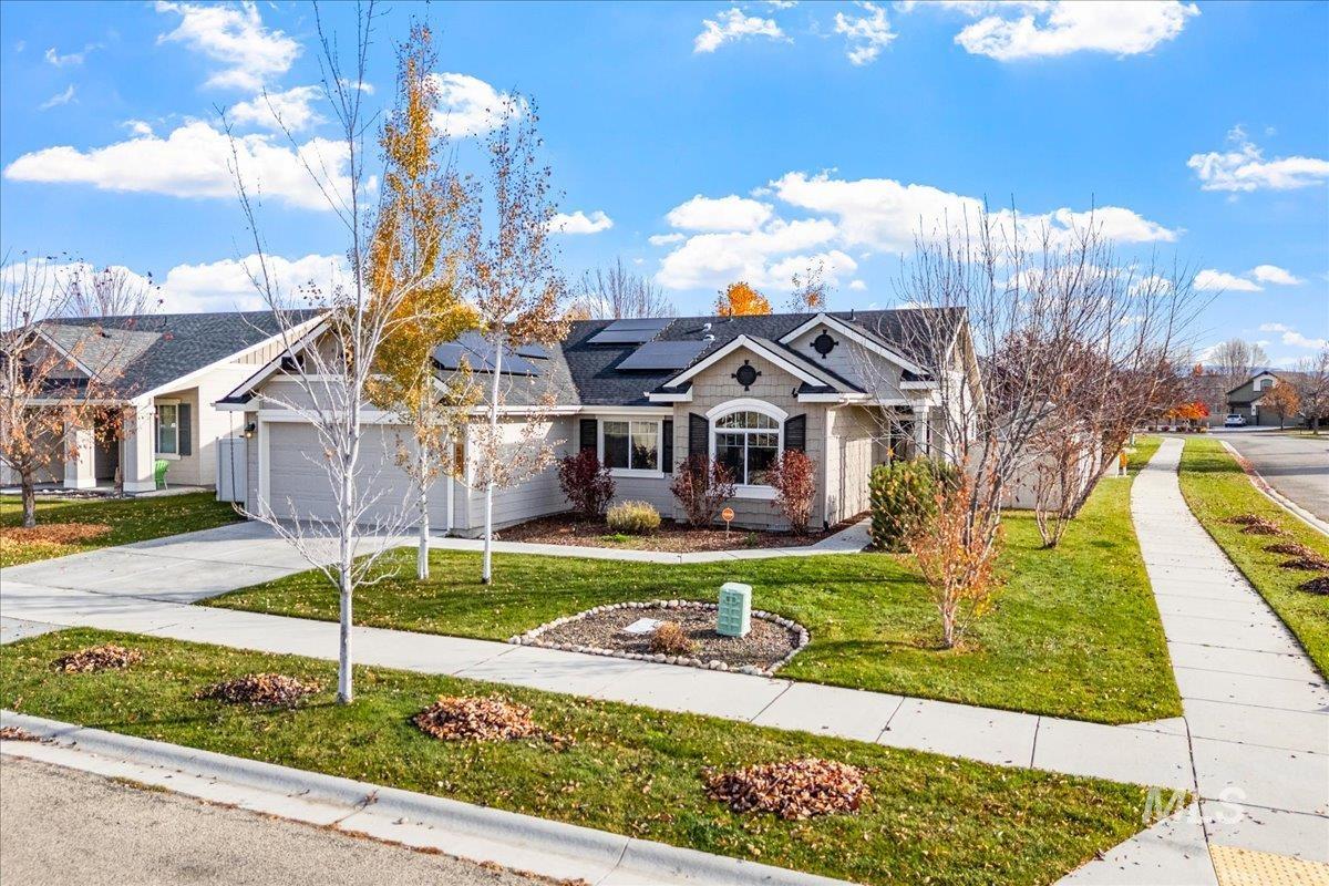 View of front of property featuring a front lawn, solar panels, driveway, and an attached garage