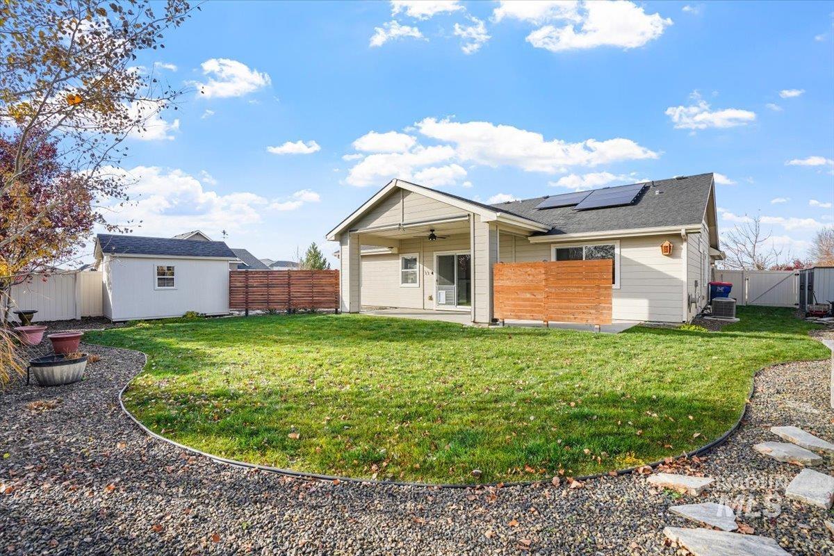 Back of property with ceiling fan, a patio, a fenced backyard, roof mounted solar panels, and an outbuilding