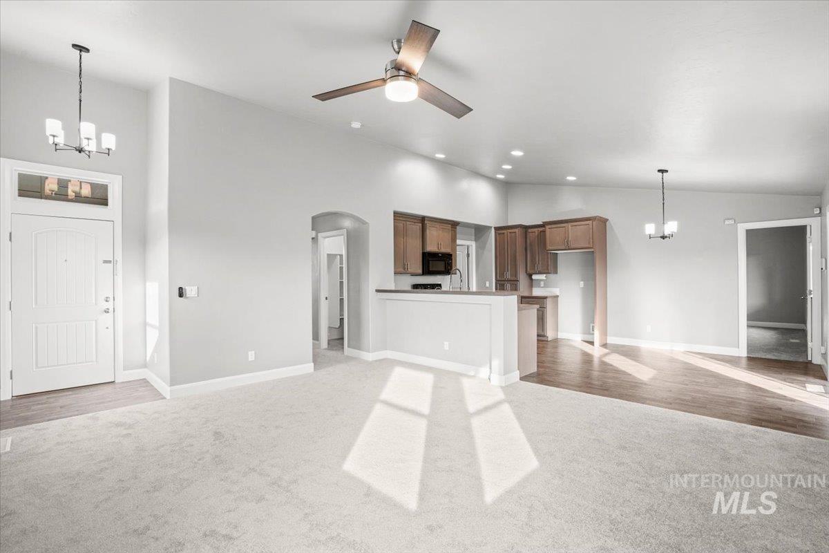 Unfurnished living room with a chandelier, light carpet, arched walkways, ceiling fan, and recessed lighting