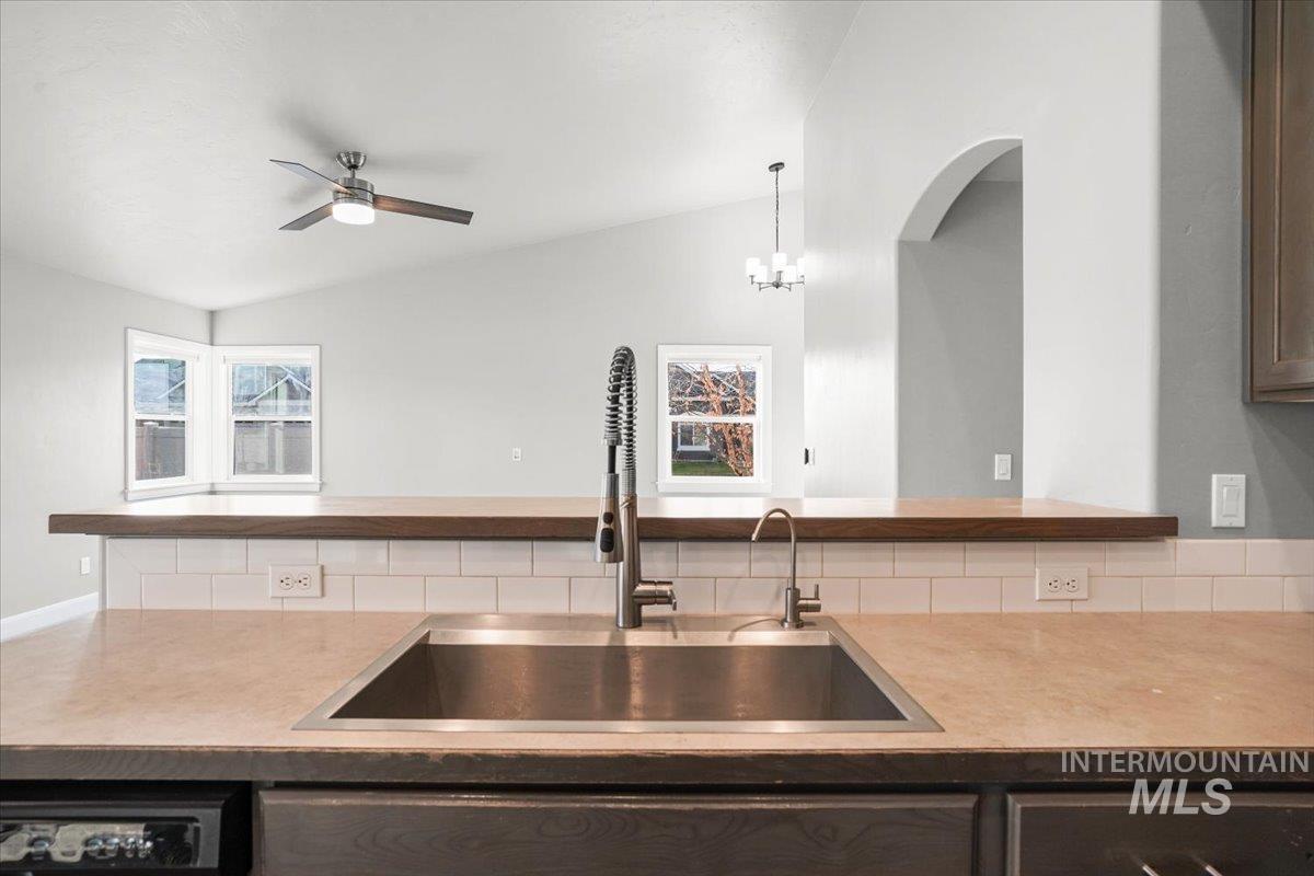 Kitchen featuring lofted ceiling, light countertops, stainless steel dishwasher, a ceiling fan, and a chandelier