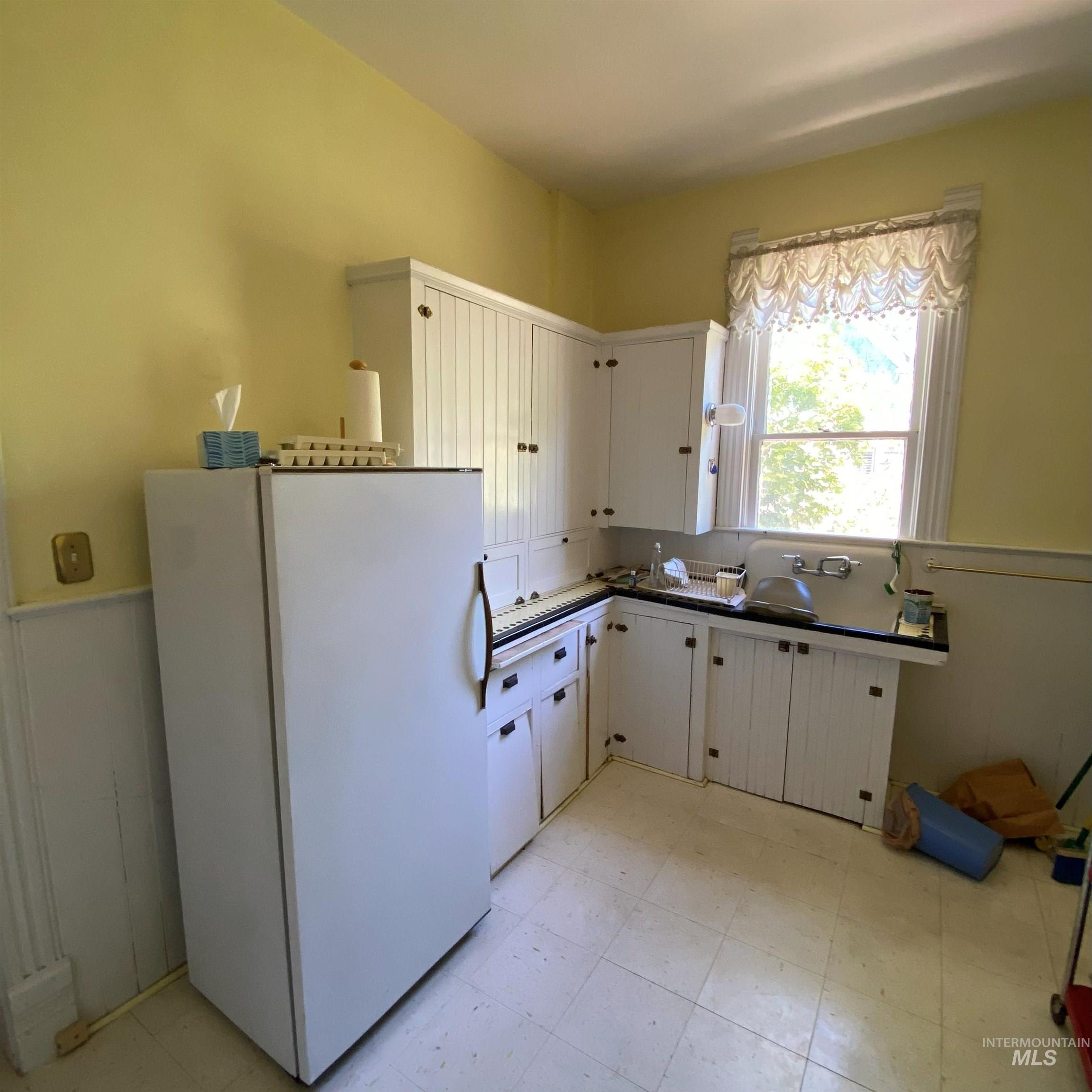 Kitchen featuring freestanding refrigerator, white cabinets, dark countertops, and light flooring