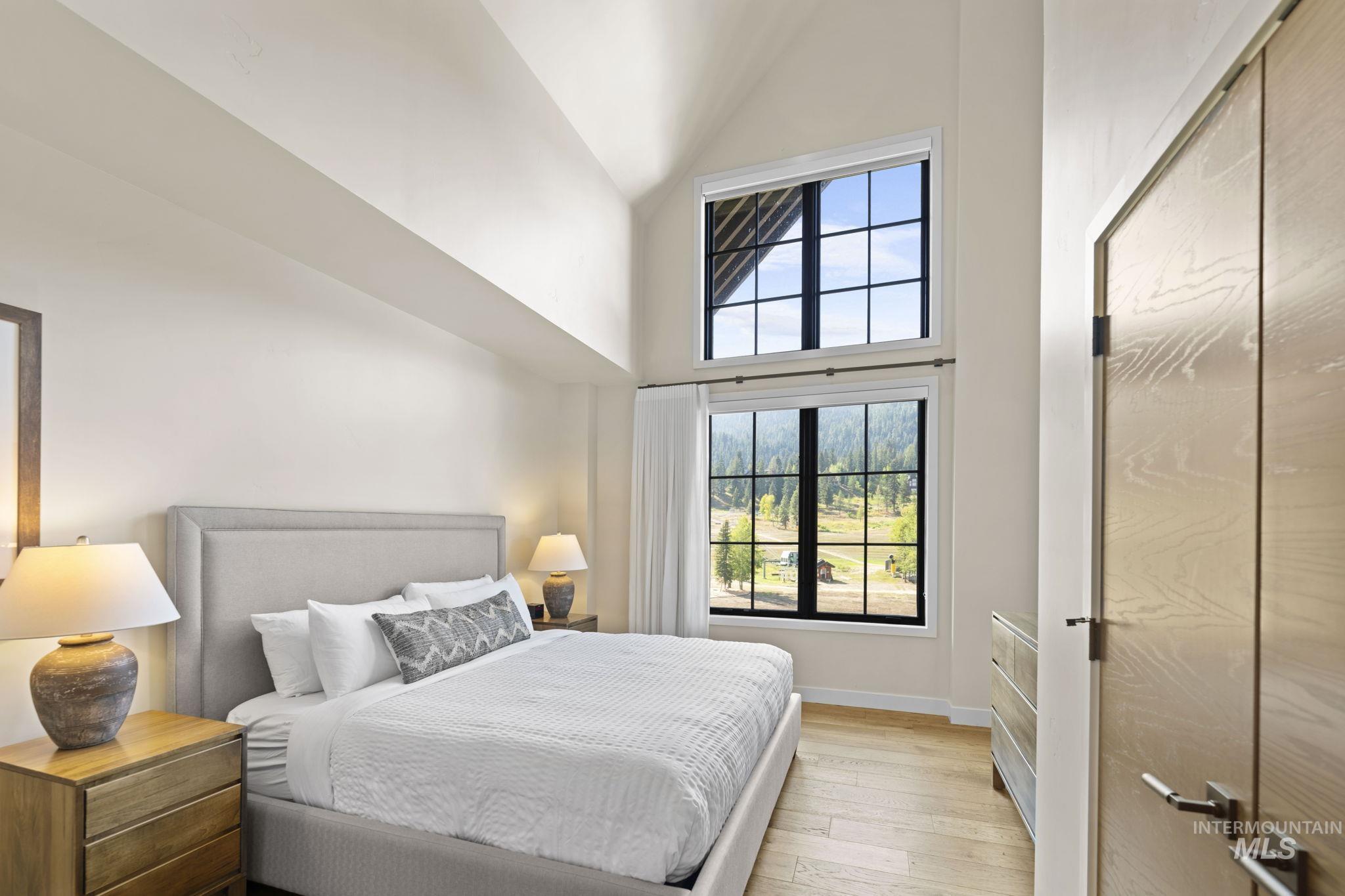Bedroom featuring multiple windows, high vaulted ceiling, and light wood-style floors