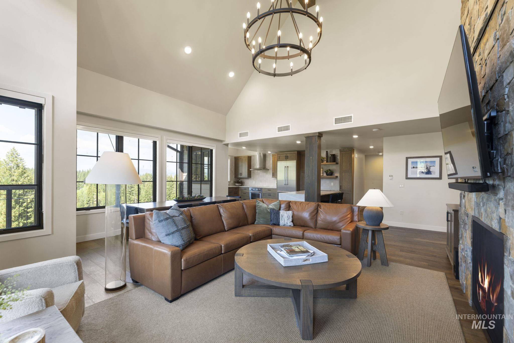 Living room with wood finished floors, high vaulted ceiling, a chandelier, a stone fireplace, and recessed lighting