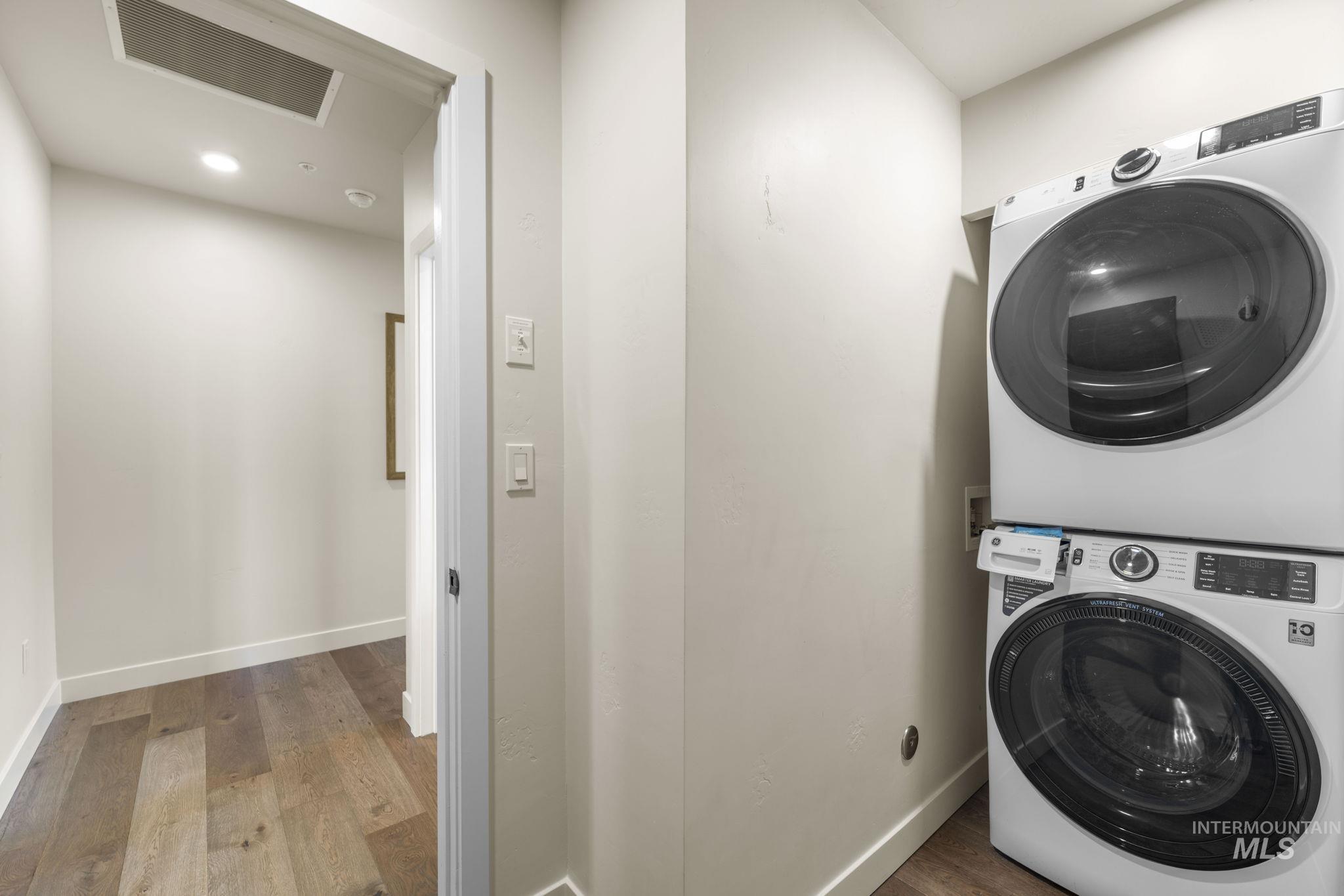 Laundry area featuring wood finished floors, stacked washing machine and dryer, and recessed lighting