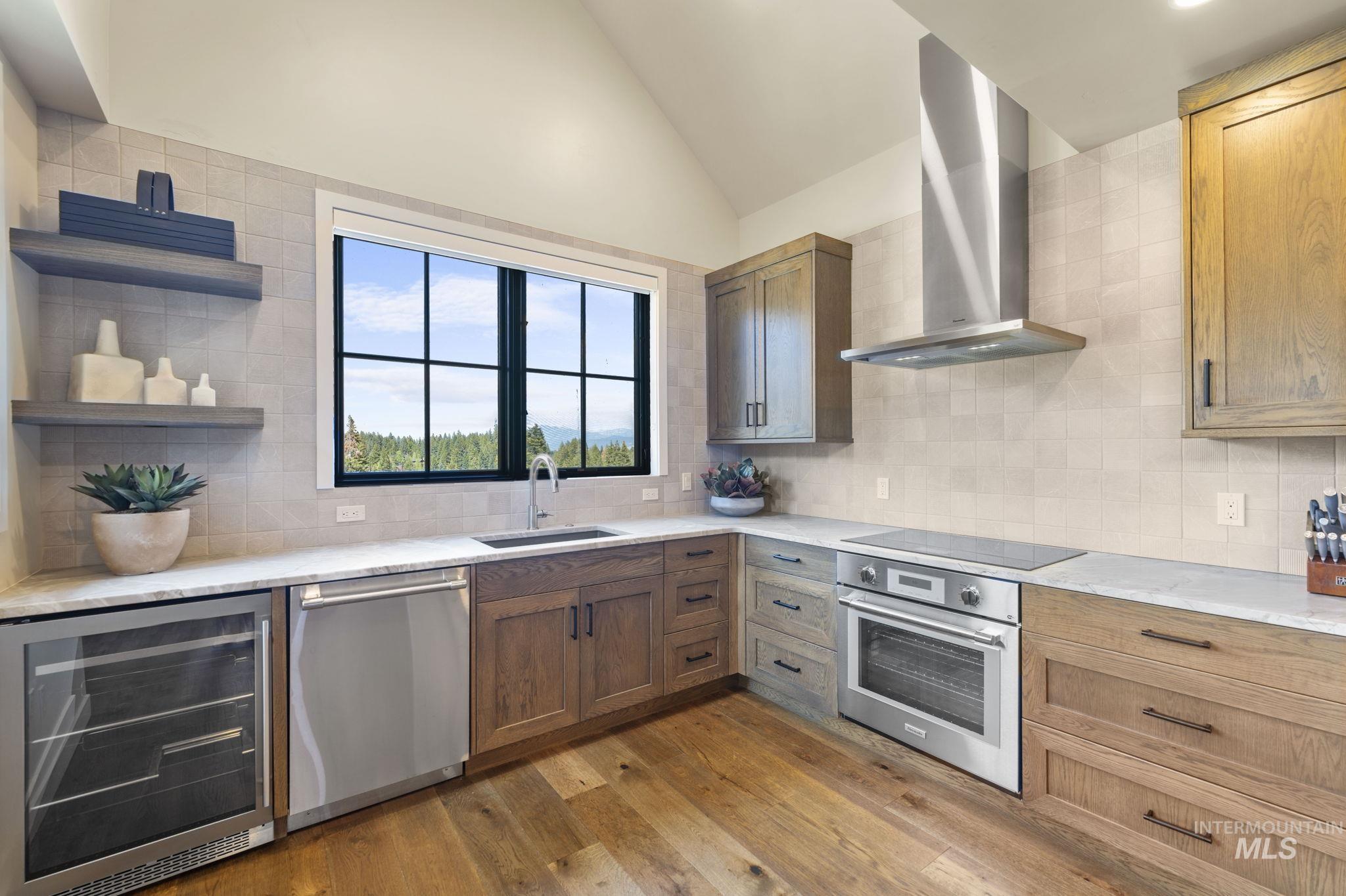 Kitchen featuring wall chimney range hood, lofted ceiling, beverage cooler, appliances with stainless steel finishes, and light wood-style floors
