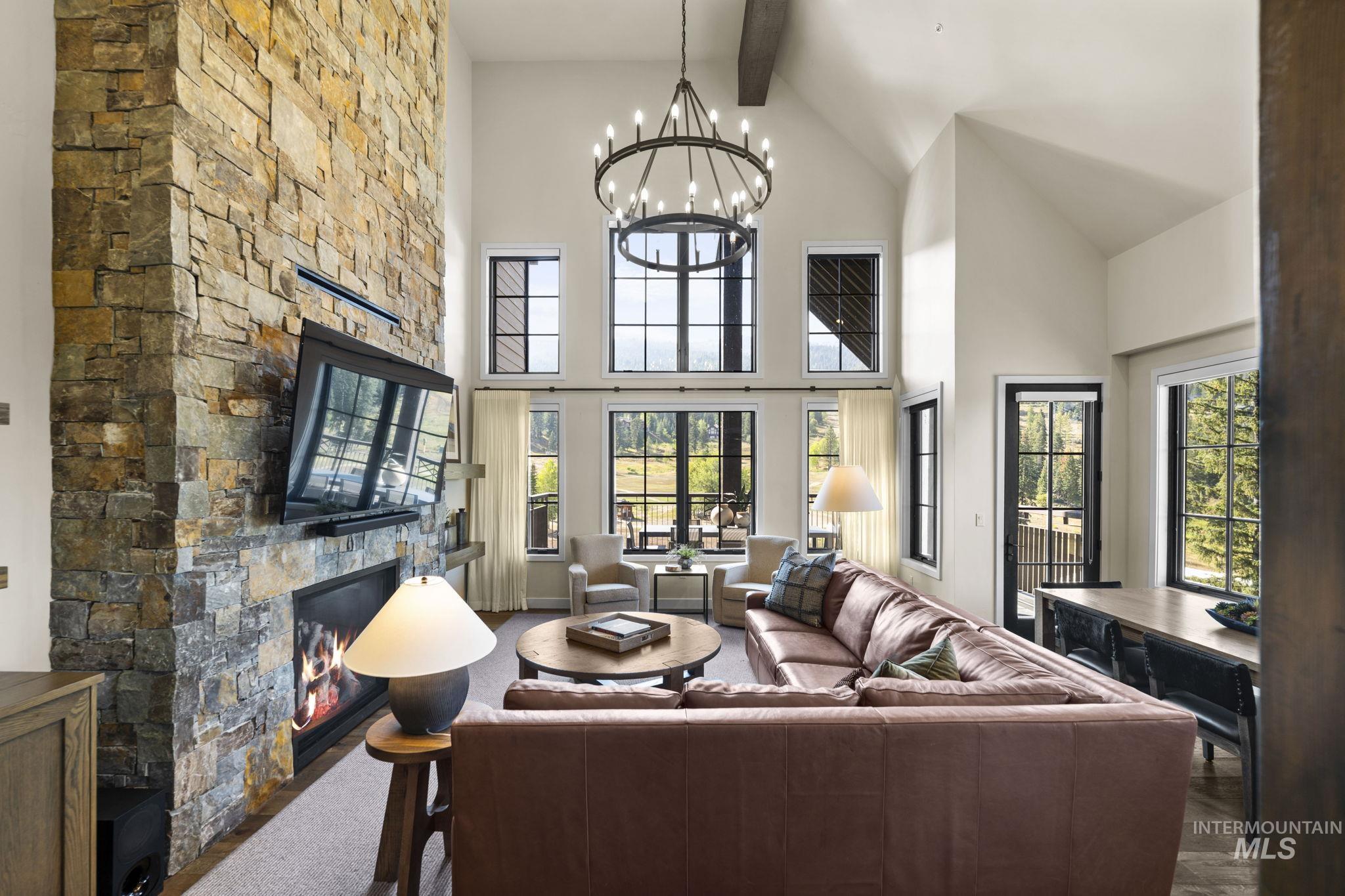 Living room with a stone fireplace, beamed ceiling, high vaulted ceiling, a chandelier, and carpet flooring