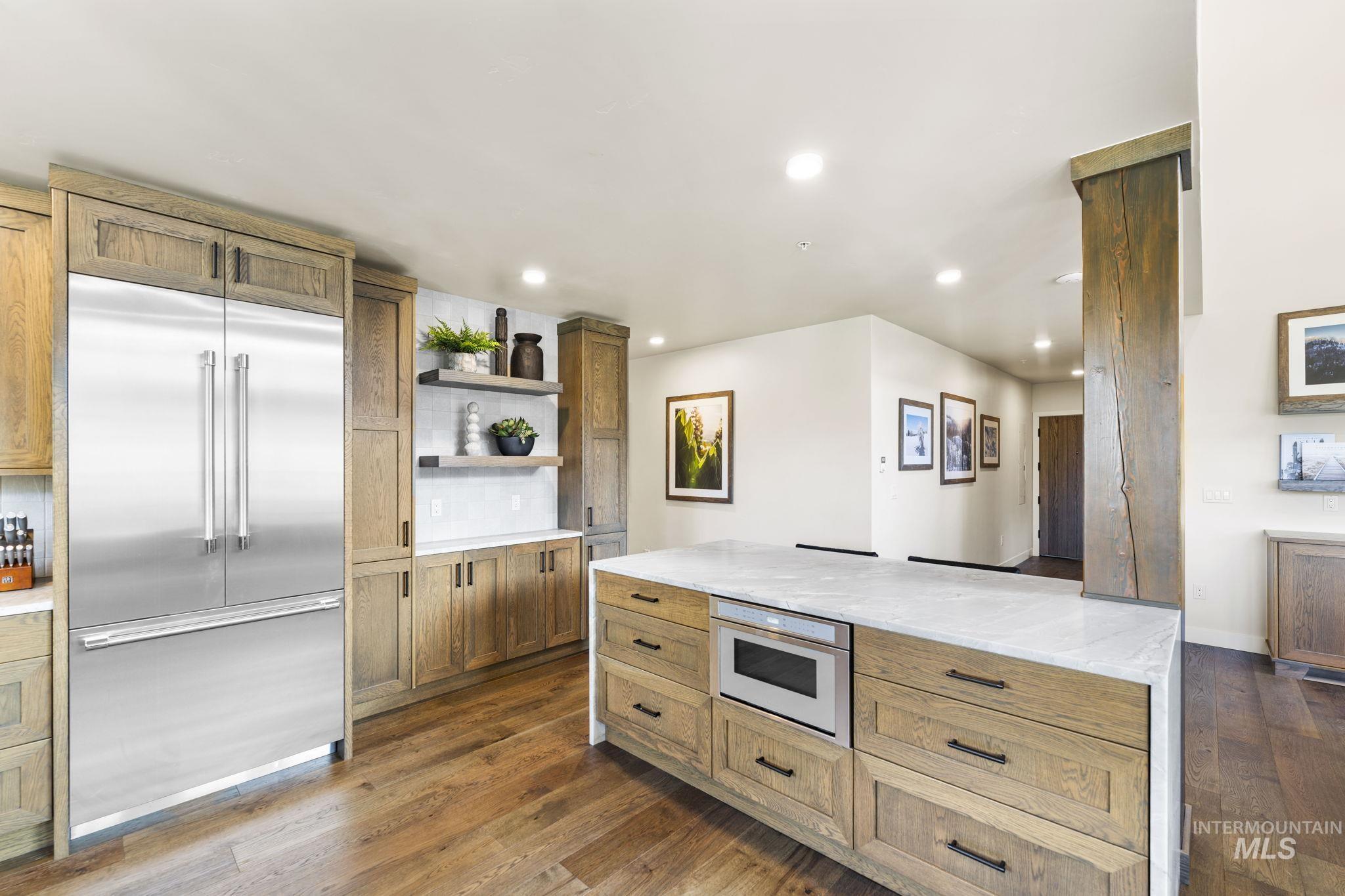 Kitchen featuring stainless steel built in fridge, open shelves, light stone counters, brown cabinets, and dark wood-style floors