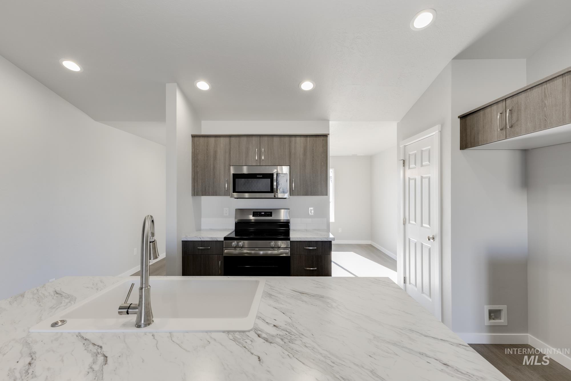 Kitchen featuring appliances with stainless steel finishes, modern cabinets, light stone counters, recessed lighting, and dark wood-style flooring