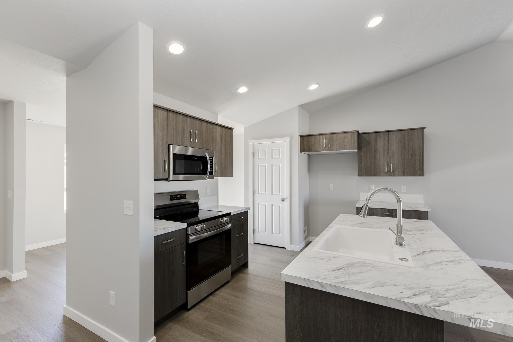 Kitchen featuring appliances with stainless steel finishes, light countertops, vaulted ceiling, dark wood-style floors, and a kitchen island with sink