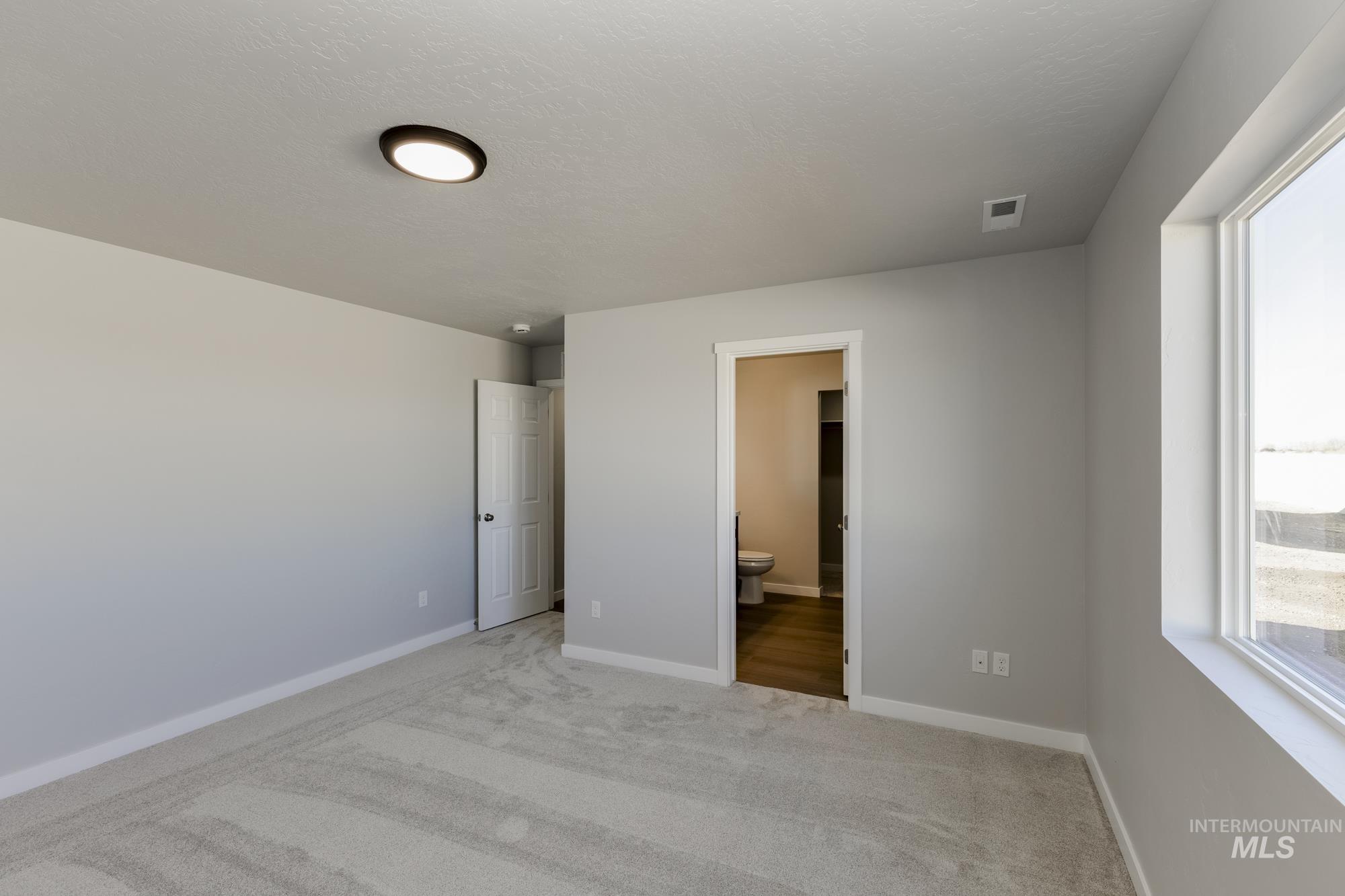 Unfurnished bedroom with carpet flooring, connected bathroom, and a textured ceiling