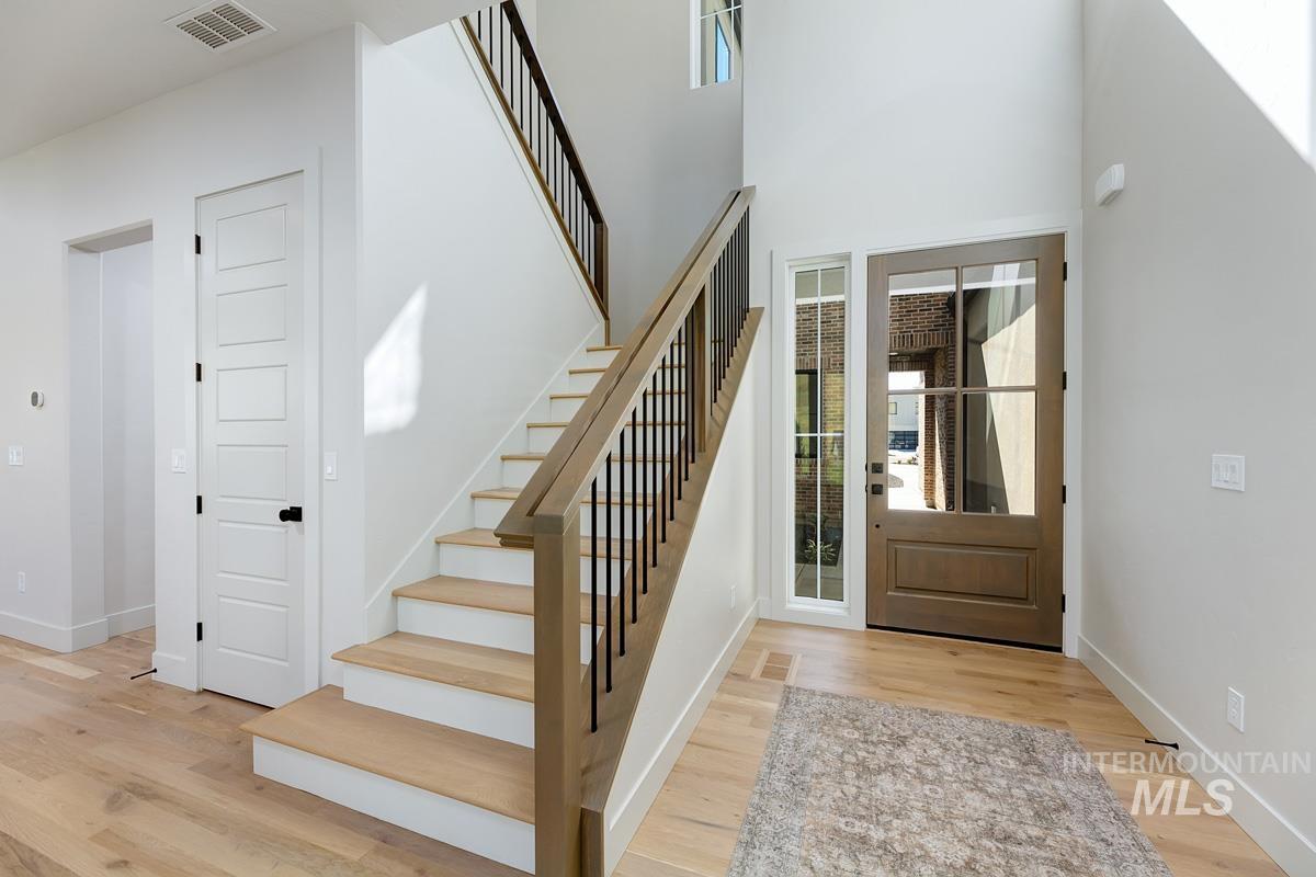Foyer entrance with healthy amount of natural light, light wood-style floors, stairway, and a towering ceiling