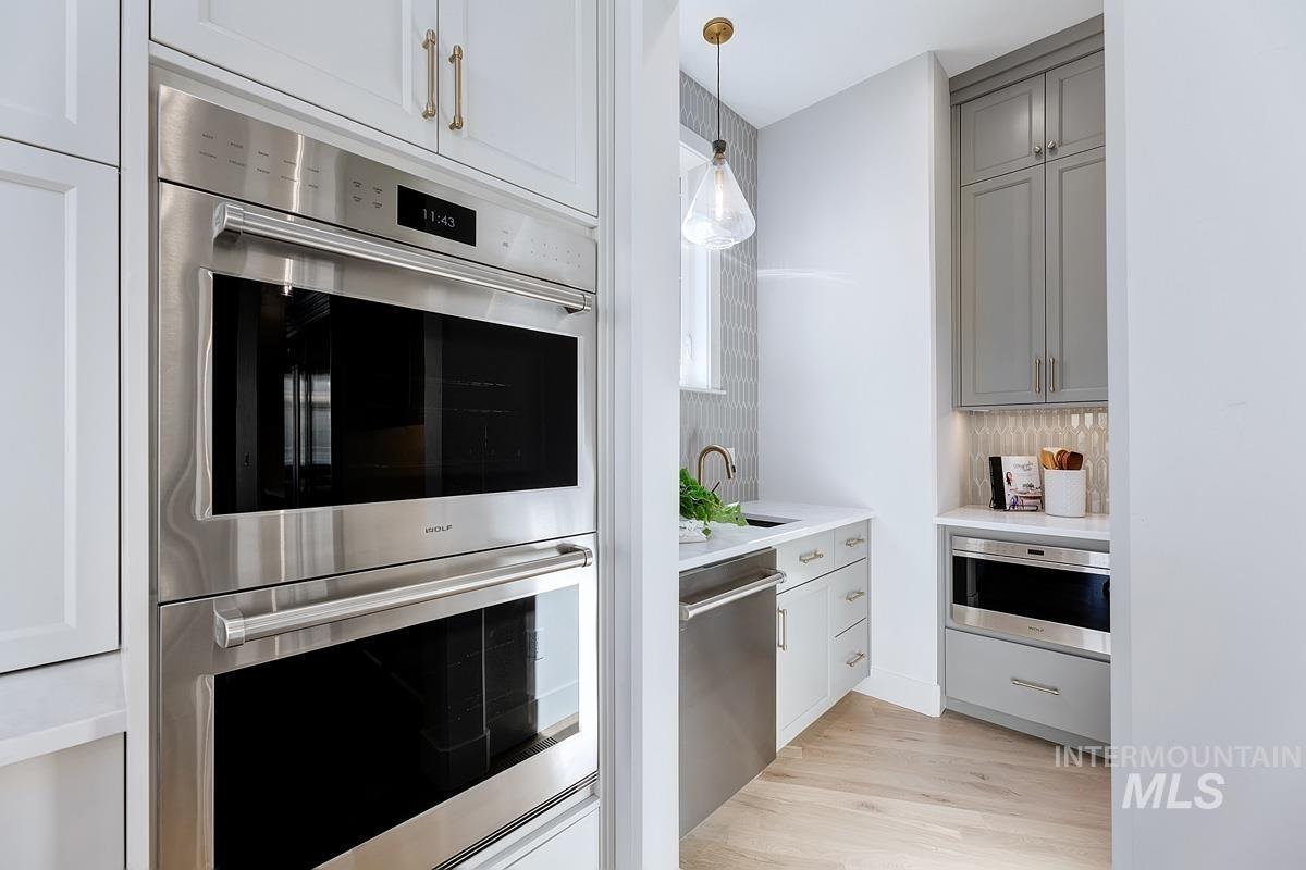 Kitchen featuring appliances with stainless steel finishes, light wood-style flooring, decorative light fixtures, gray cabinetry, and light stone countertops