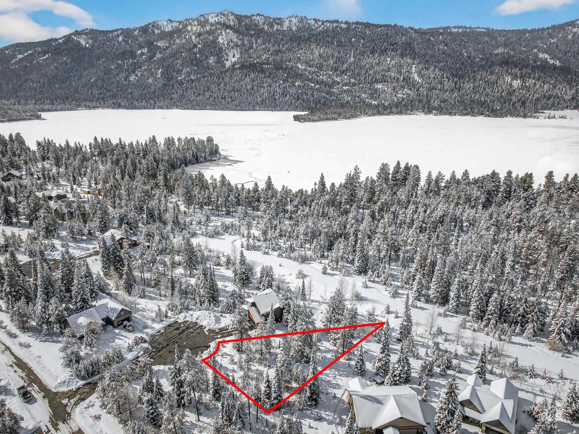 Snowy aerial view with a mountain view, property parcel outlined, and a view of trees