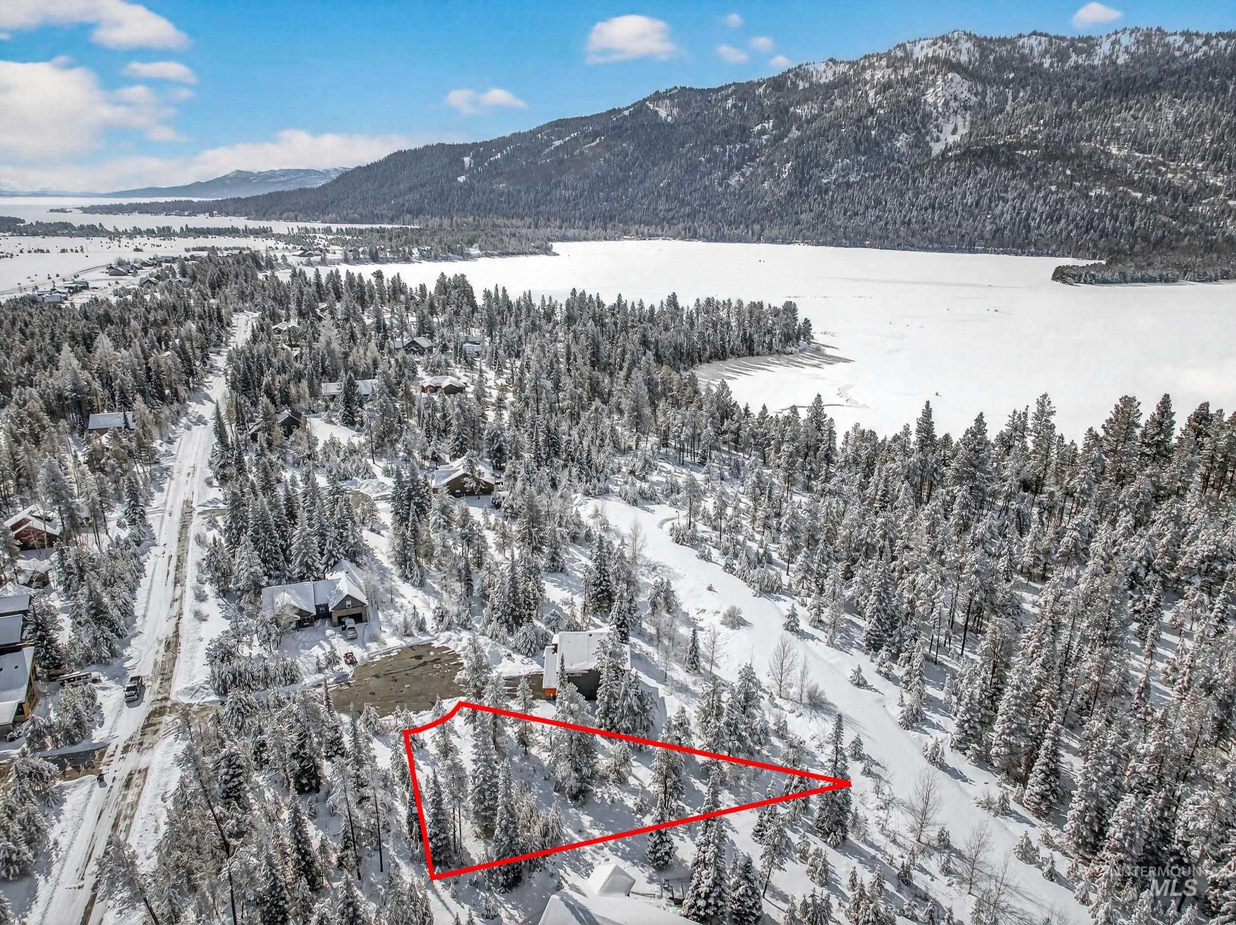 Snowy aerial view with property parcel outlined, a mountain view, and a forest view
