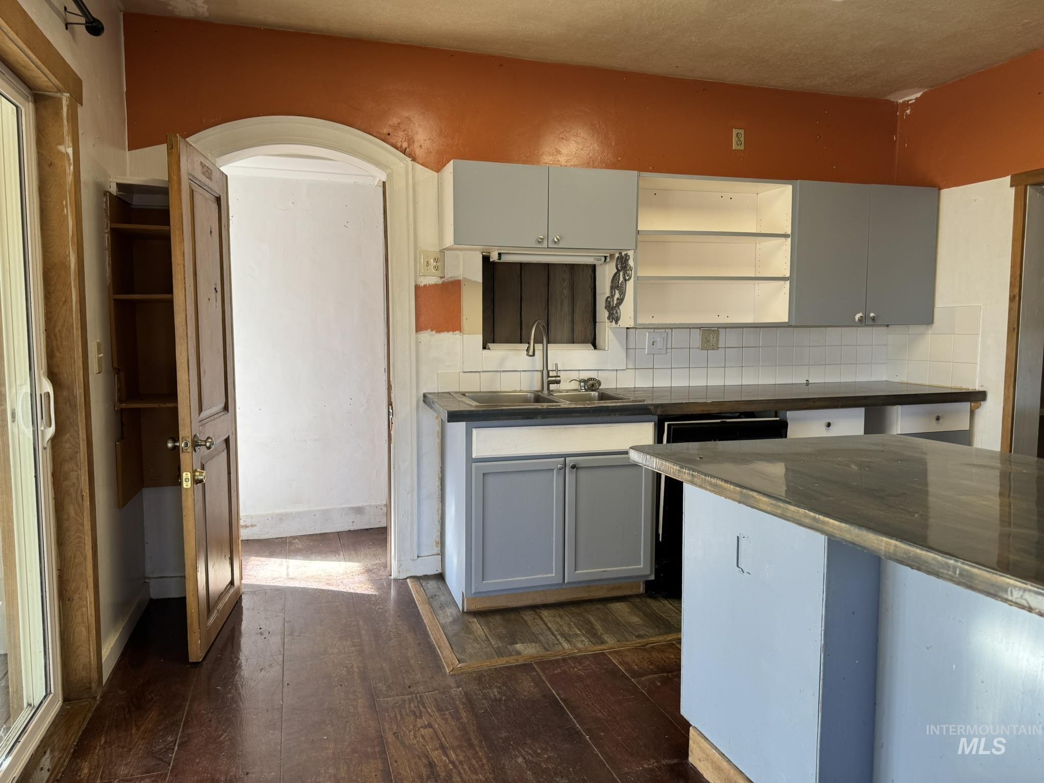 Kitchen featuring open shelves, gray cabinetry, dark wood-type flooring, dark countertops, and backsplash
