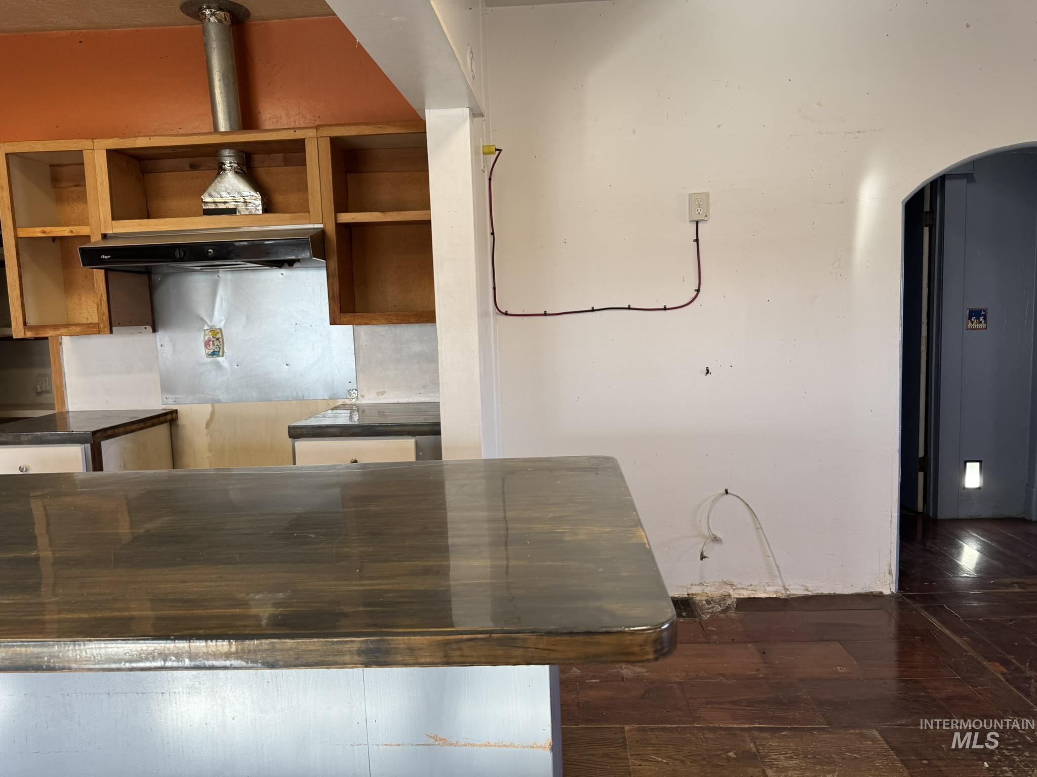 Kitchen with arched walkways, under cabinet range hood, dark wood-style floors, and brown cabinets