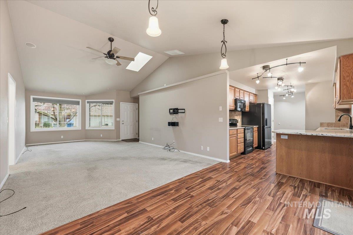Kitchen featuring open floor plan, a skylight, decorative light fixtures, black appliances, and dark carpet