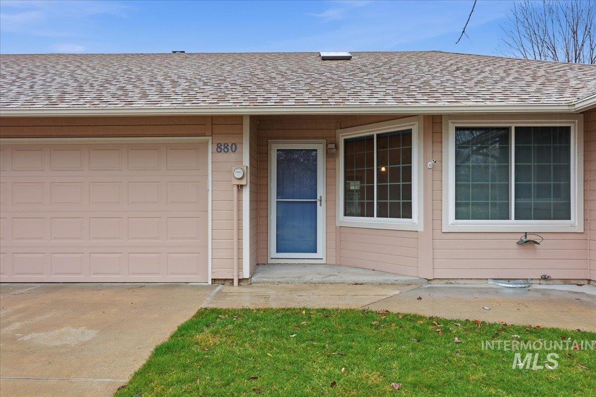 Entrance to property featuring roof with shingles, concrete driveway, and a patio