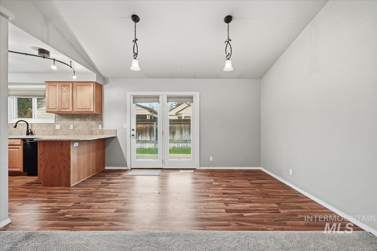 Kitchen with hanging light fixtures, tasteful backsplash, dark wood-type flooring, and a peninsula