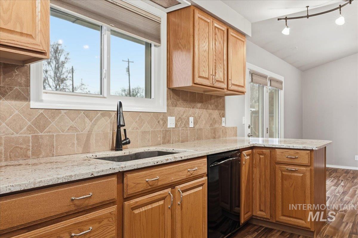 Kitchen featuring light stone counters, dishwasher, dark wood finished floors, and a peninsula