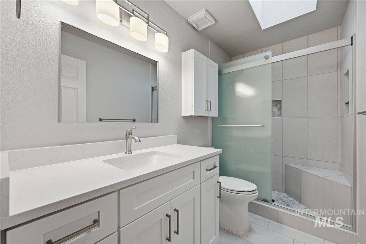 Bathroom featuring a skylight, vanity, a stall shower, and light tile patterned floors
