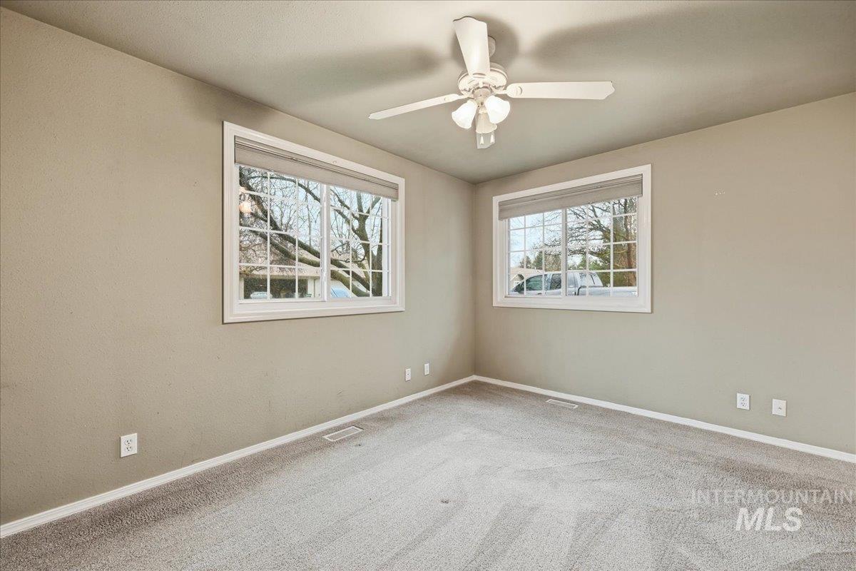Carpeted empty room featuring plenty of natural light and ceiling fan
