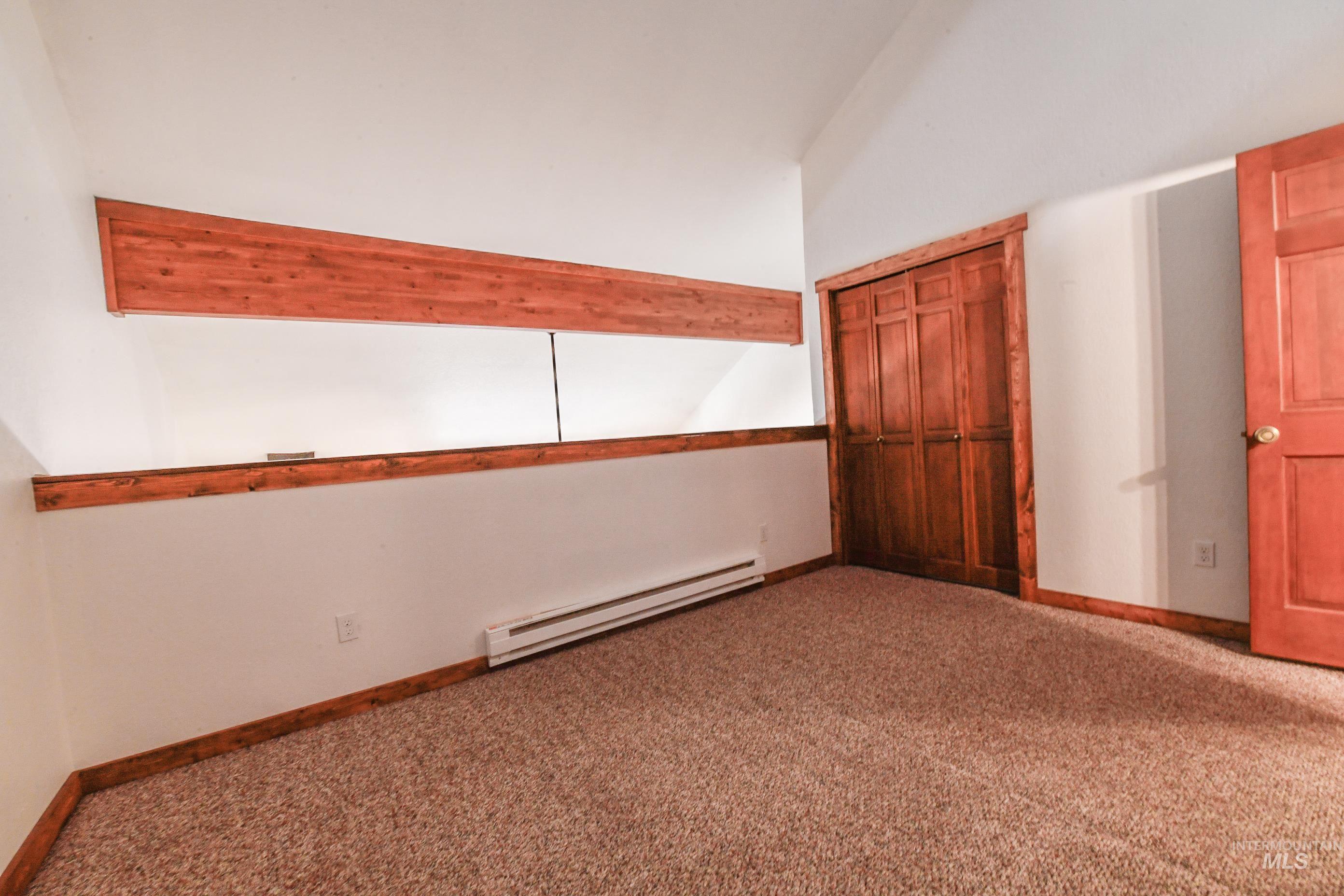 Empty room featuring a baseboard heating unit, carpet flooring, and vaulted ceiling