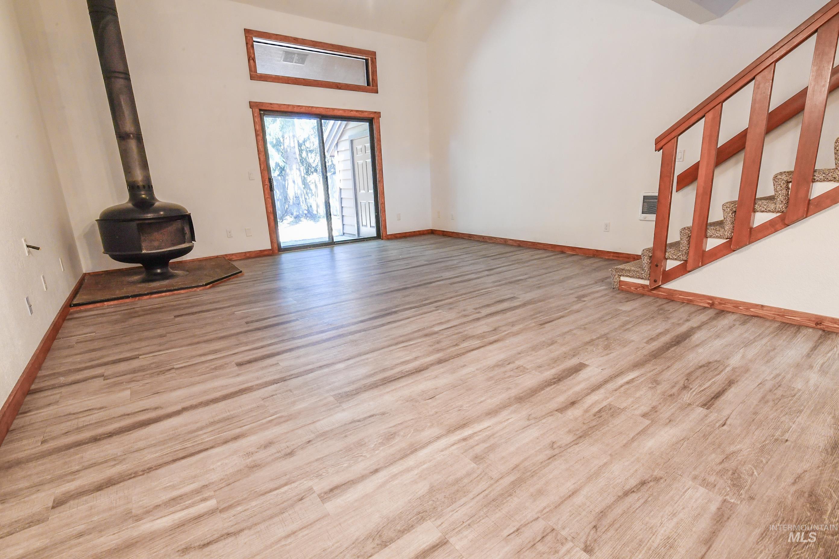 Unfurnished living room featuring wood finished floors, a wood stove, and a towering ceiling