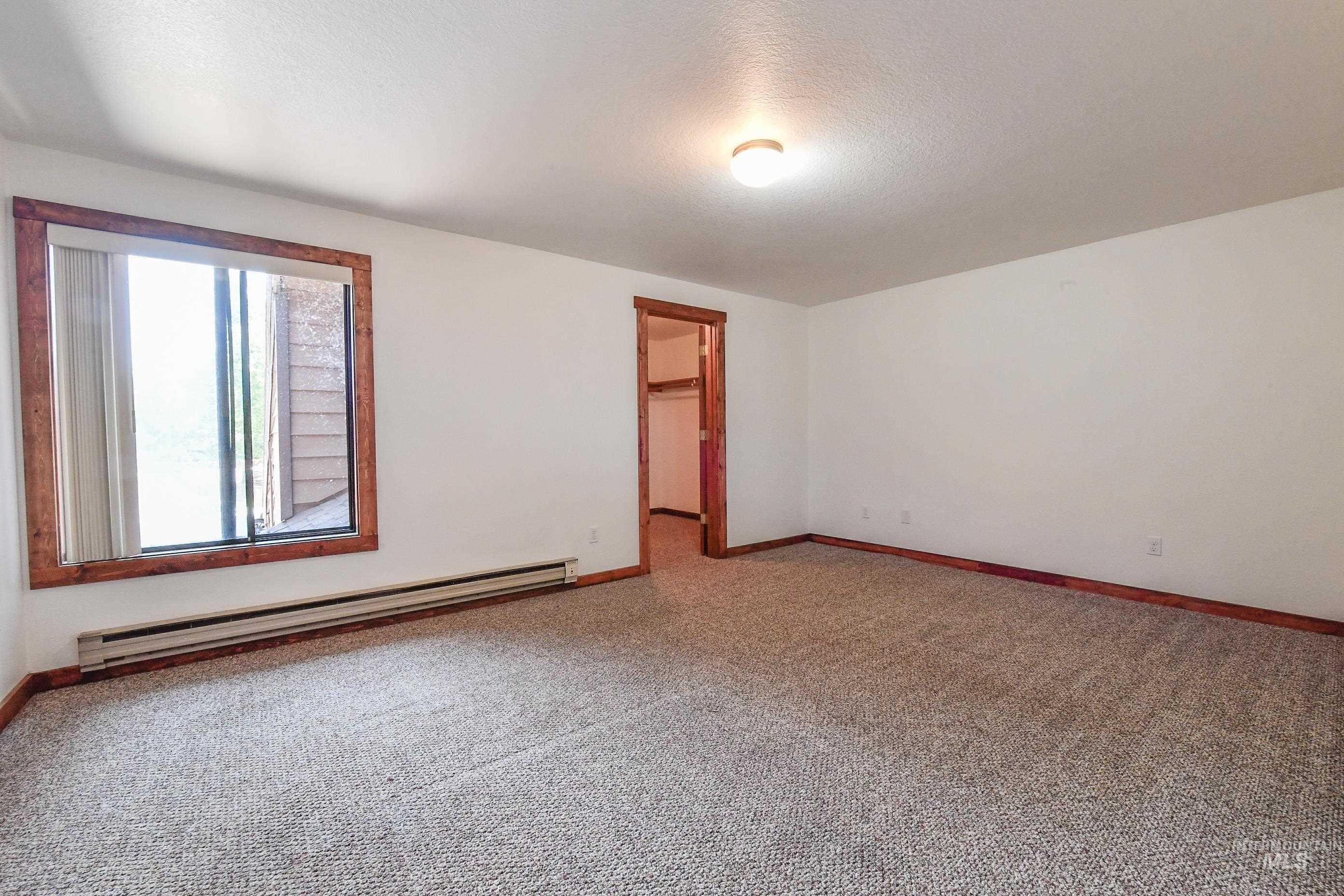 Carpeted spare room with a baseboard heating unit and baseboards