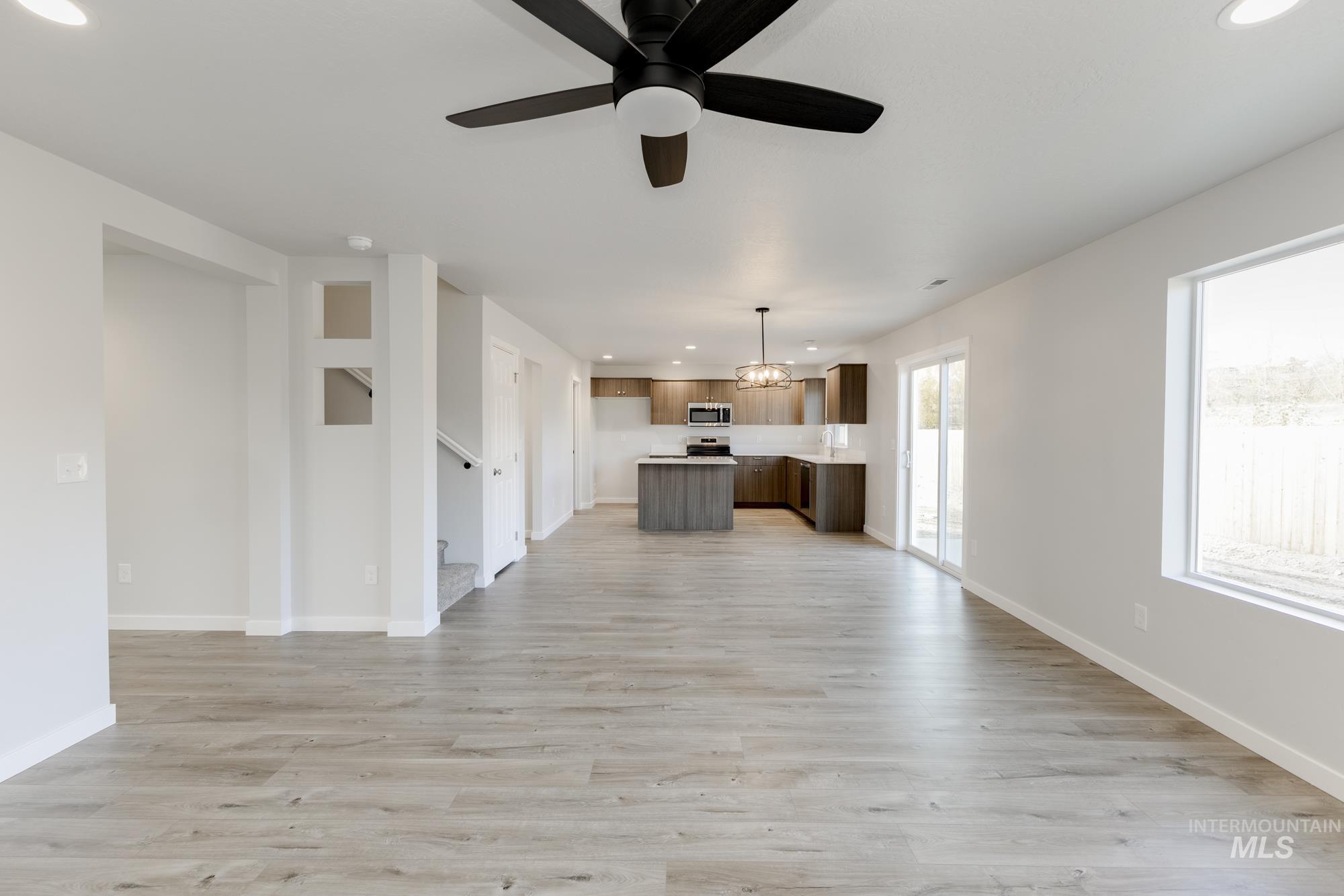Unfurnished living room featuring recessed lighting, light wood-style flooring, ceiling fan, and a chandelier