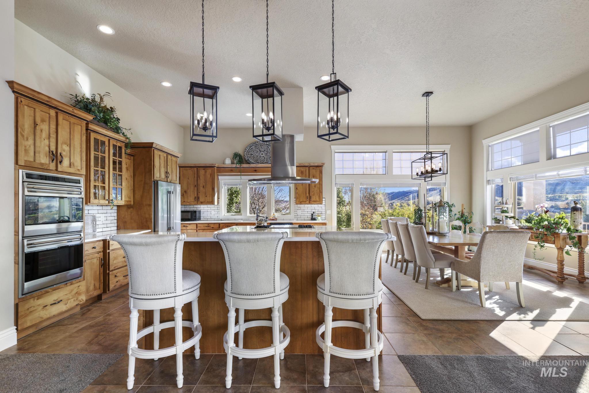 Kitchen with brown cabinets, glass insert cabinets, decorative backsplash, decorative light fixtures, and stainless steel appliances